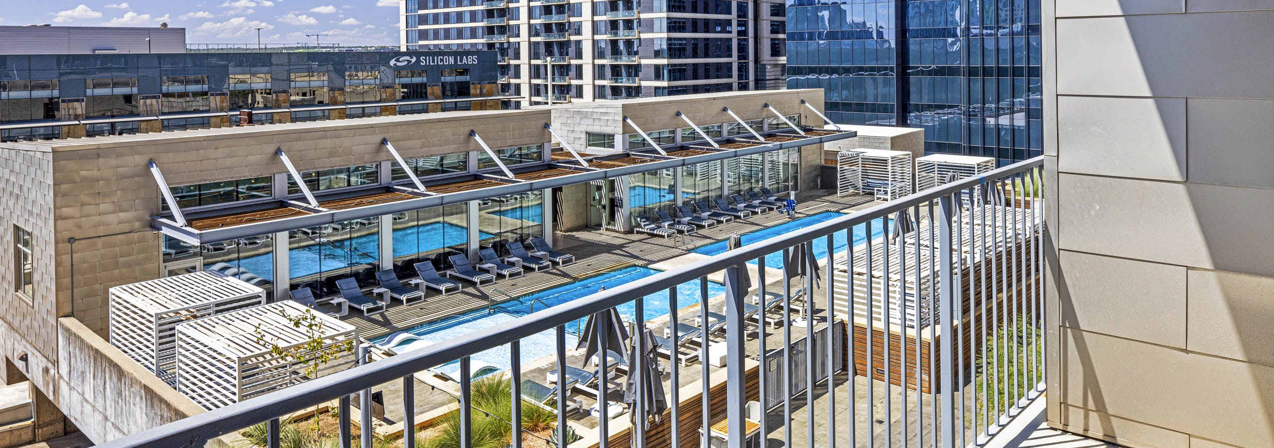 View of rooftop pool and lounge chairs from apartment balcony above at AMLI on 2nd with blue sky and city buildings