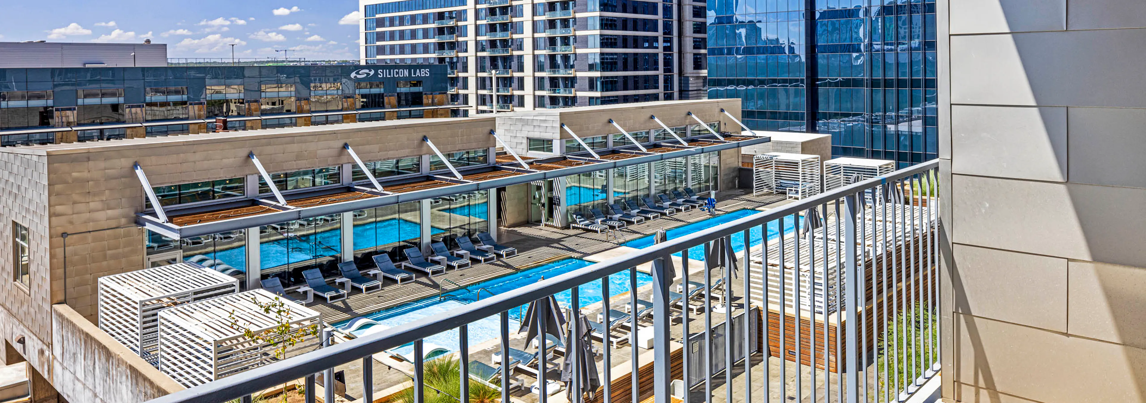 View of rooftop pool  and lounge chairs from apartment balcony above at AMLI on 2nd with blue sky and city buildings