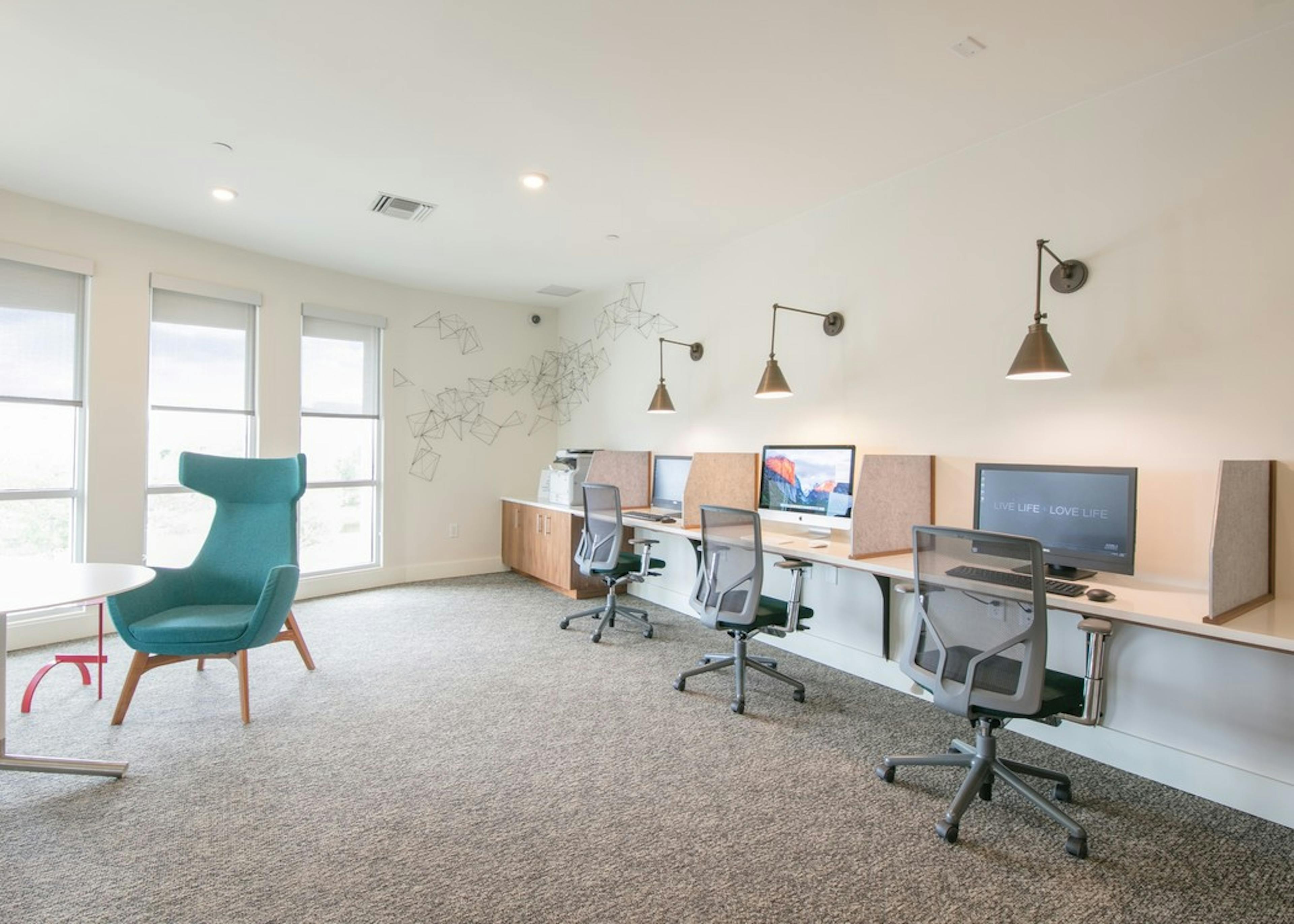 A business center at AMLI Dry Creek apartments with several computers and rolling desk chairs as well as additional seating
