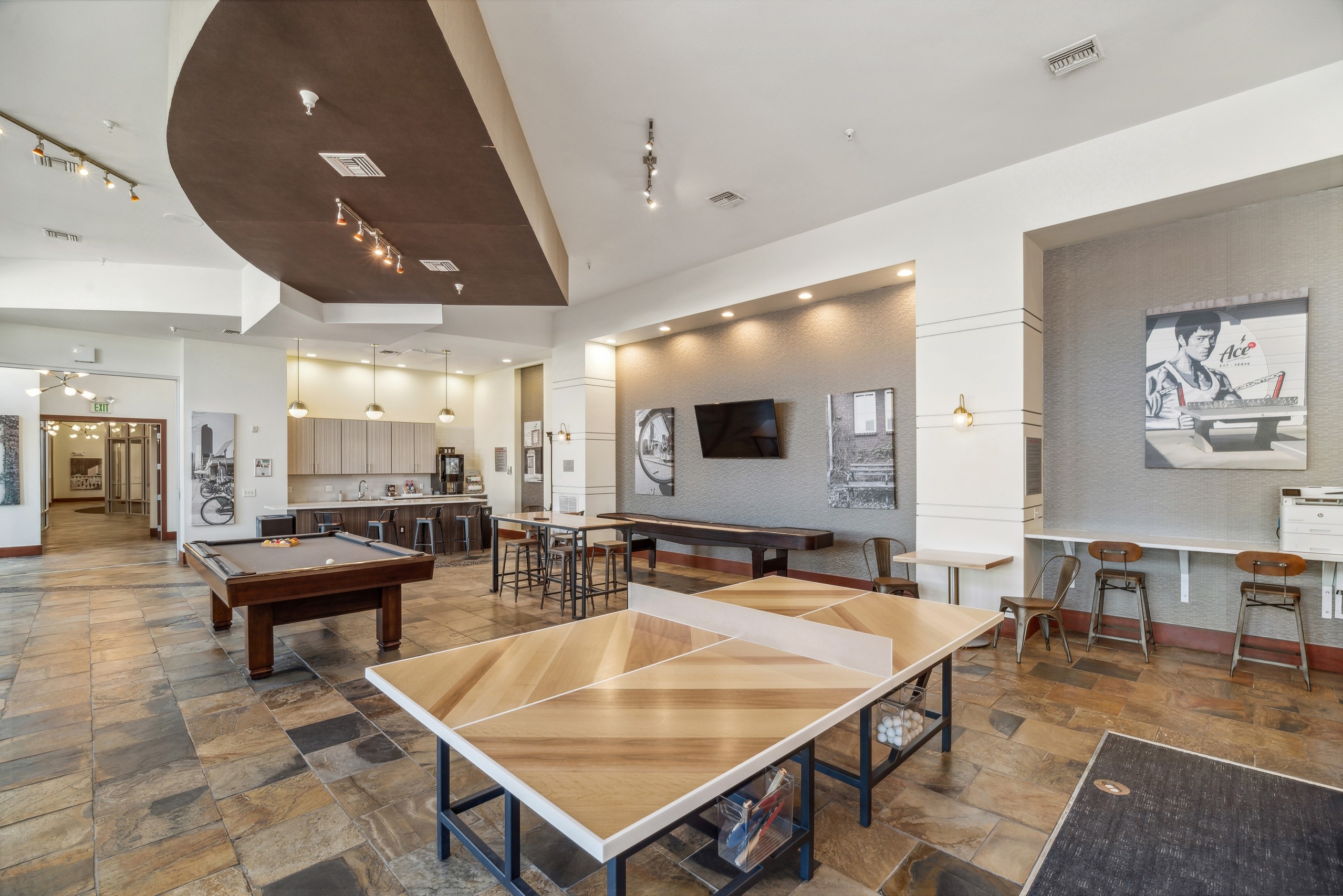 View of the clubroom at AMLI Park Avenue with a shuffle board table and ping pong table and a television and kitchen area