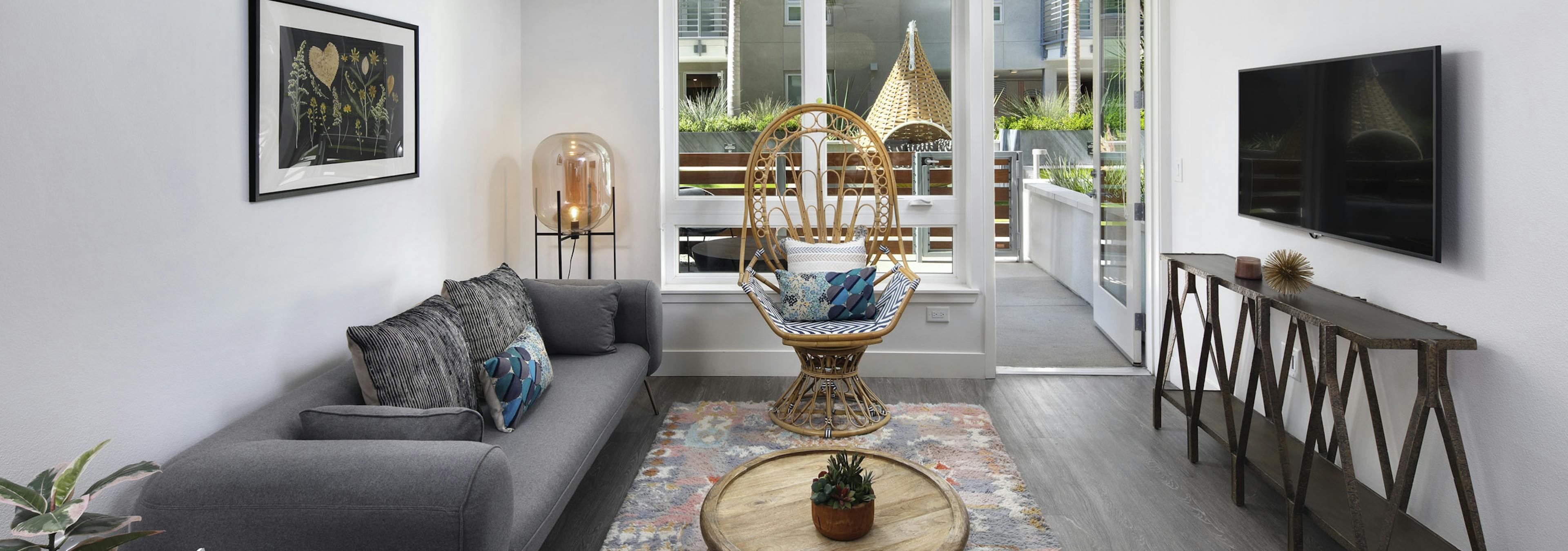 AMLI Park Broadway apartment living room with grey couch and wicker chair in front of large window overlooking patio