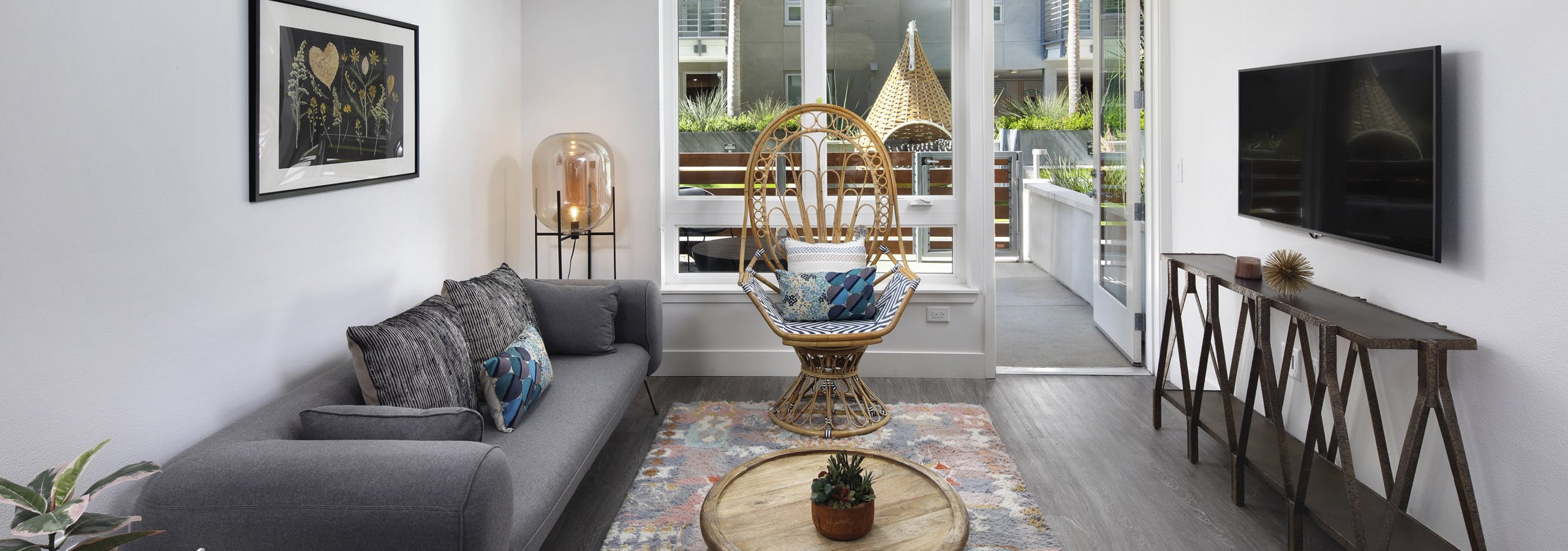 AMLI Park Broadway apartment living room with grey couch and wicker chair in front of large window overlooking patio