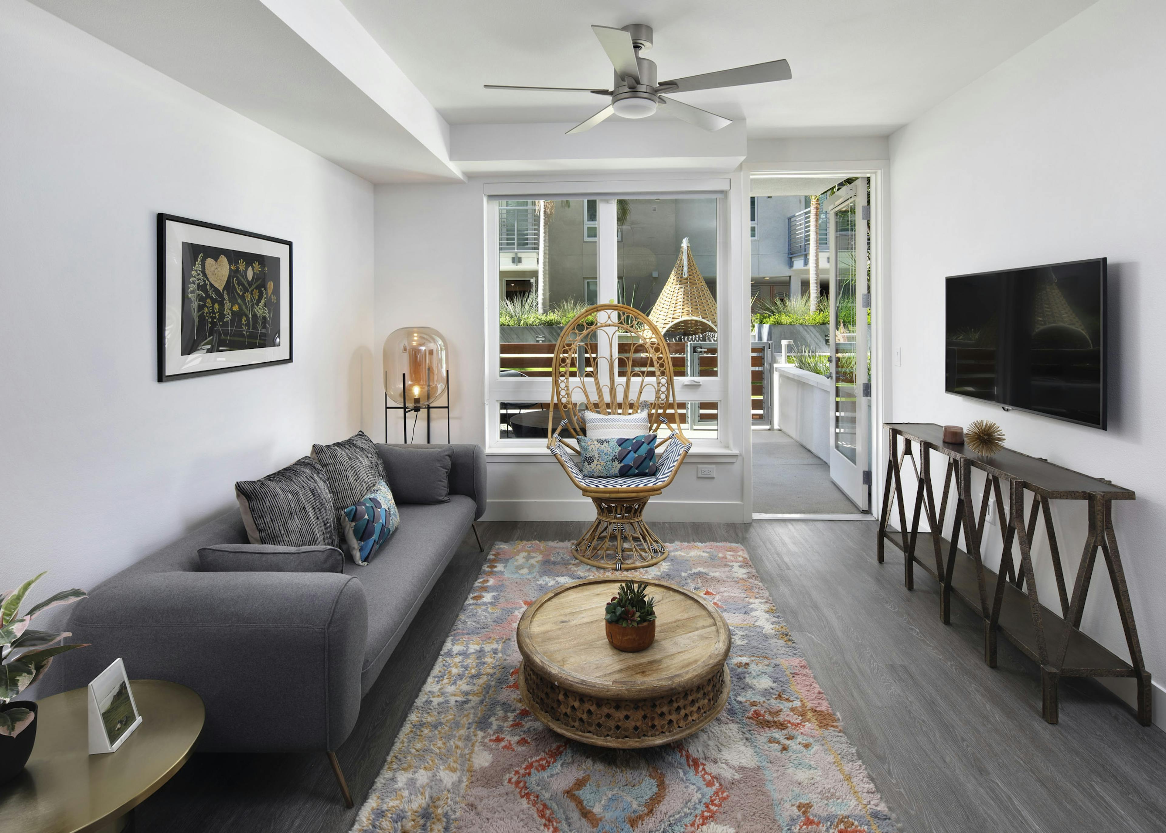 AMLI Park Broadway apartment living room with grey couch and wicker chair in front of large window overlooking patio
