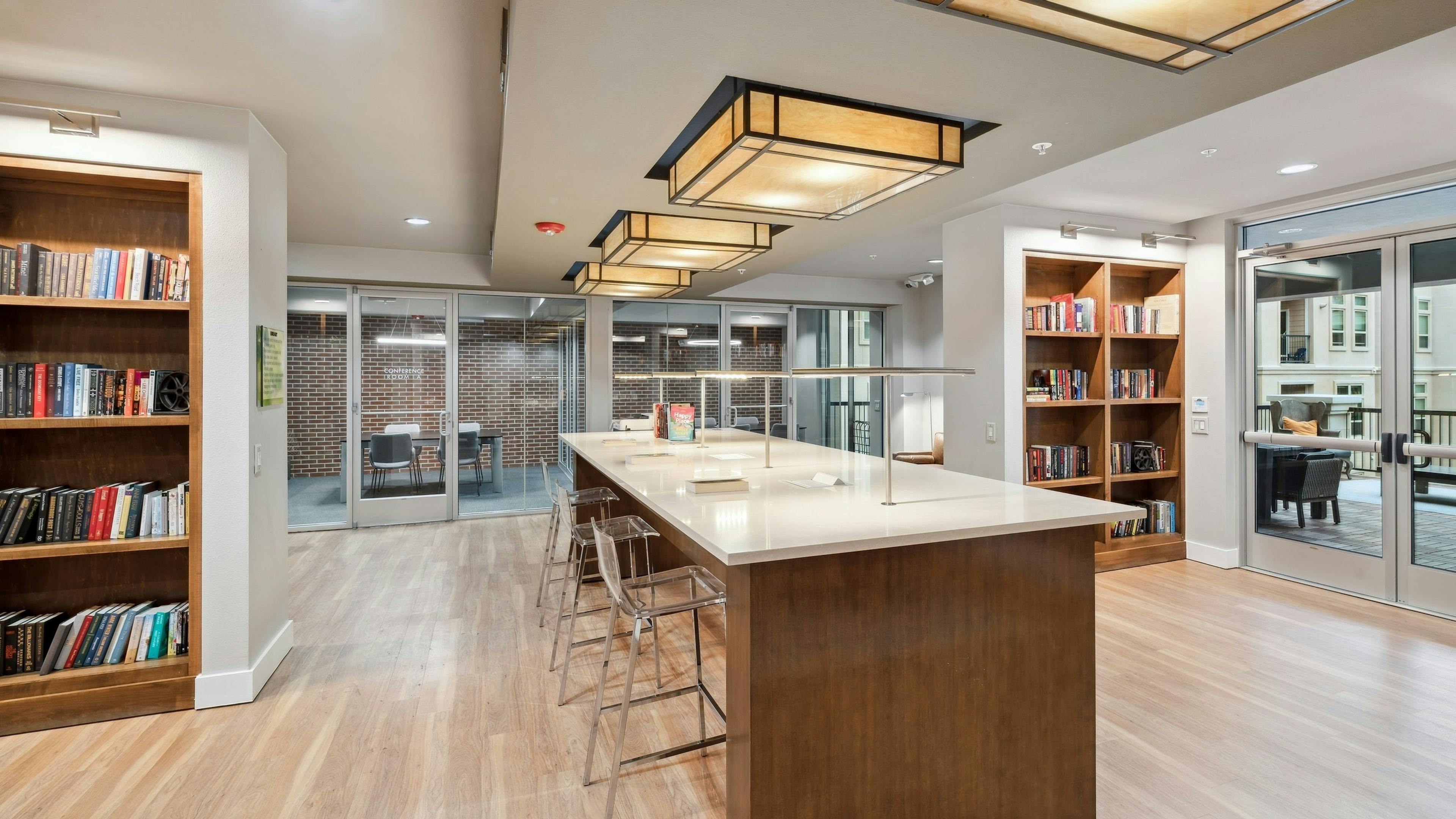 A library at AMLI RidgeGate with wooden table with acrylic chairs and filled bookshelves and overhead lighting
