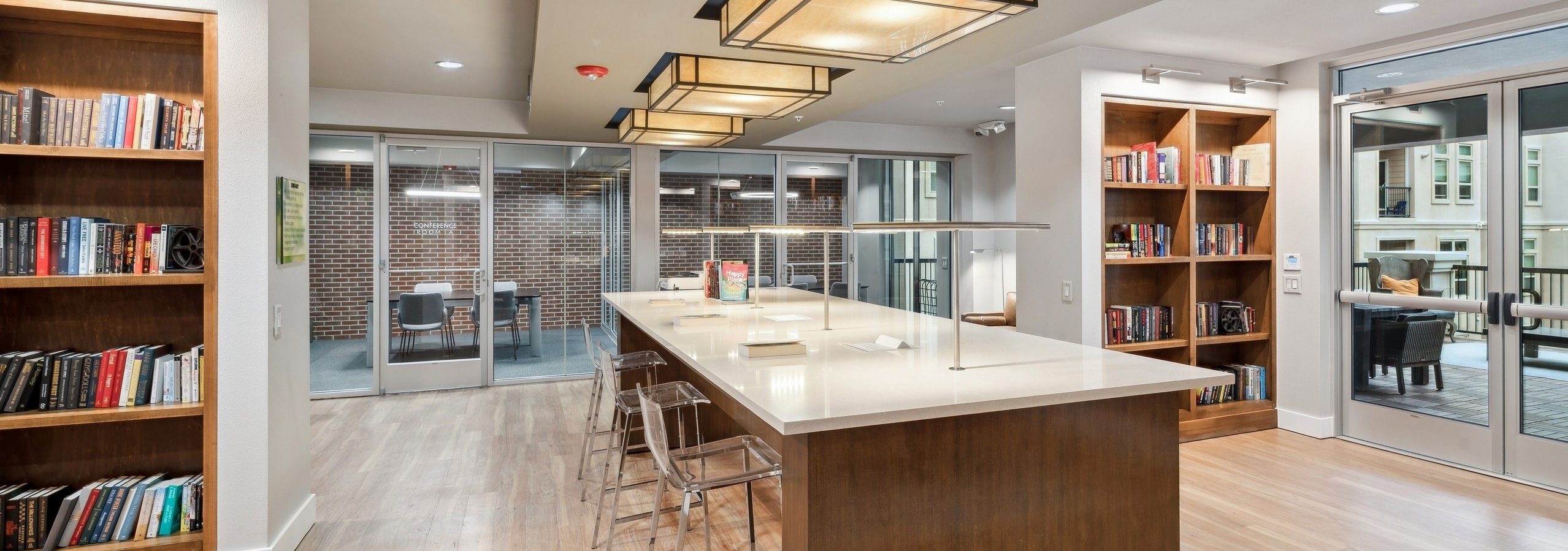 A library at AMLI RidgeGate with wooden table with acrylic chairs and filled bookshelves and overhead lighting