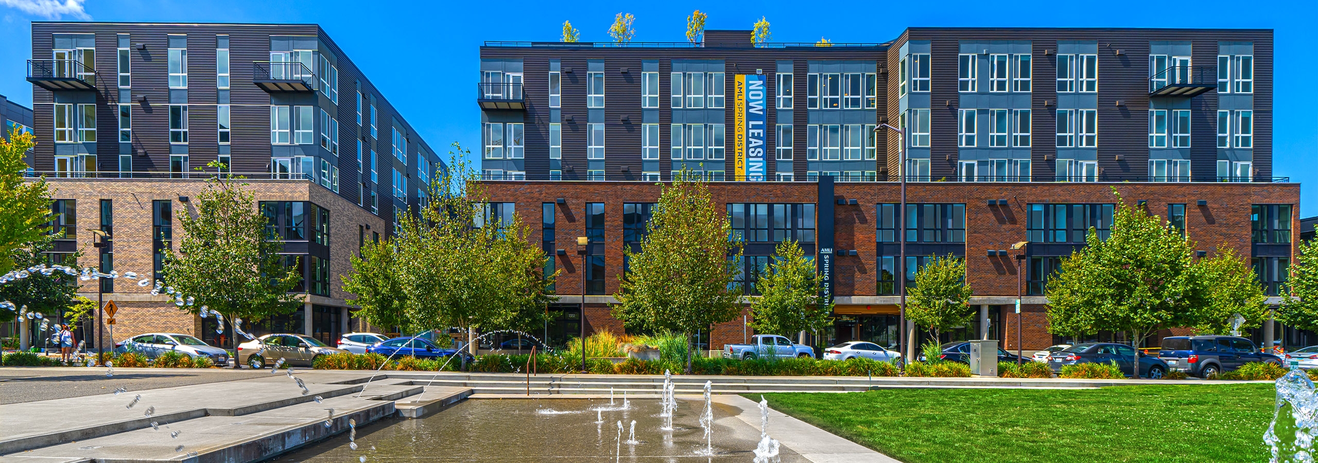 AMLI Spring District brick apartment building with water fountain and grass in foreground and cars and trees lining street