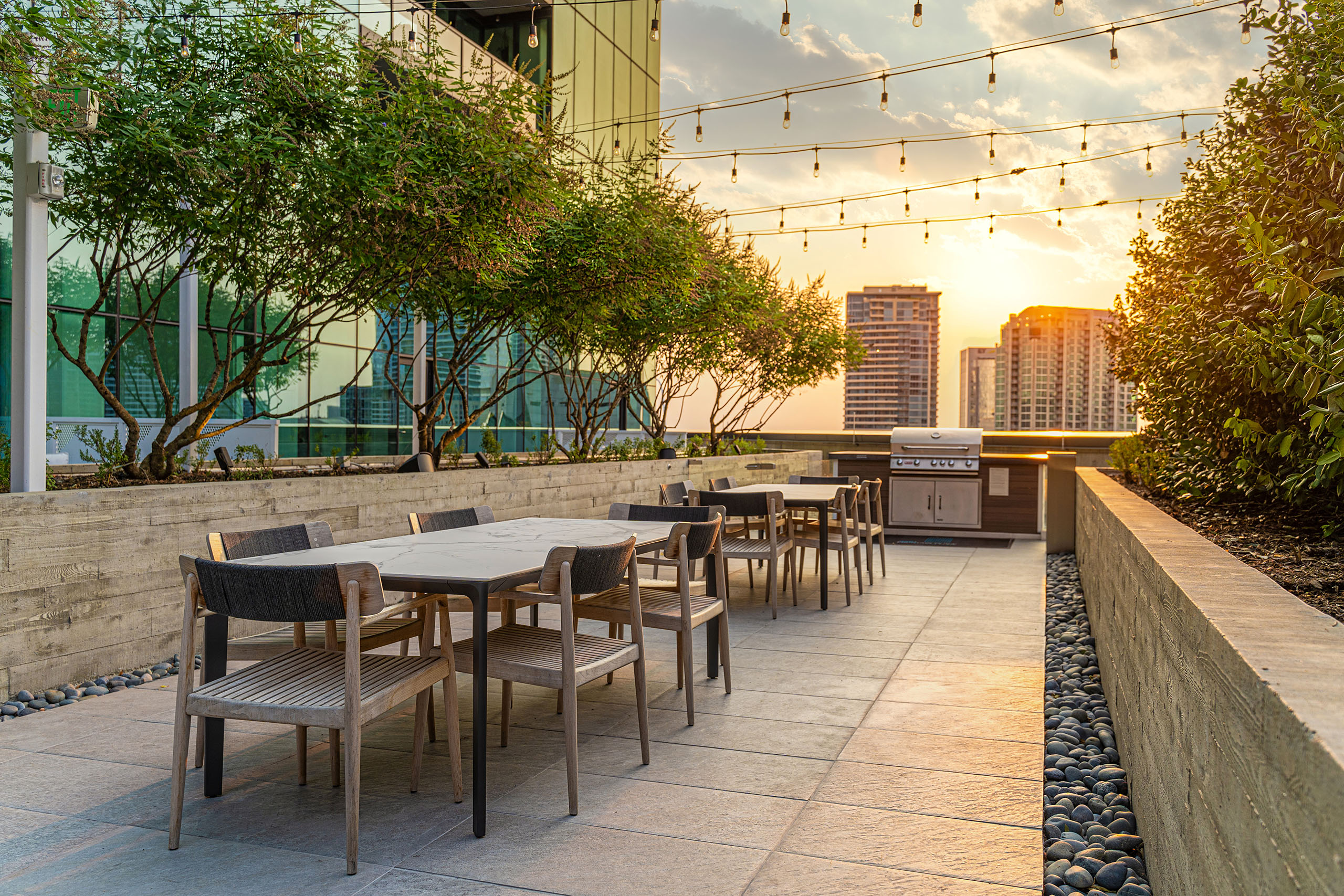 AMLI Fountain Place outdoor dining area with two white marble top tables with chairs near grill under hanging lights