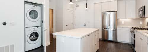 Interior of AMLI Park Broadway apartment kitchen with white cabinetry, stainless steel appliances and full washer and dryer