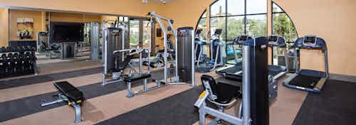 Interior view of AMLI Spanish HIlls fitness center with flat screen TV, cardio equipment and free weights facing courtyard