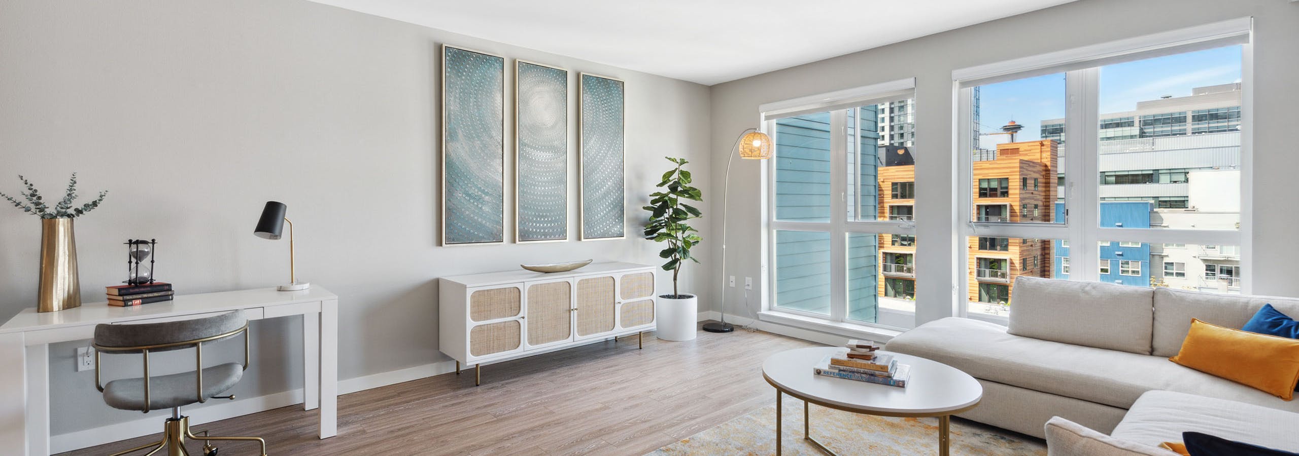 AMLI 535 living room with view of city and desk and sideboard with artwork and couch and multi color carpet with coffee table