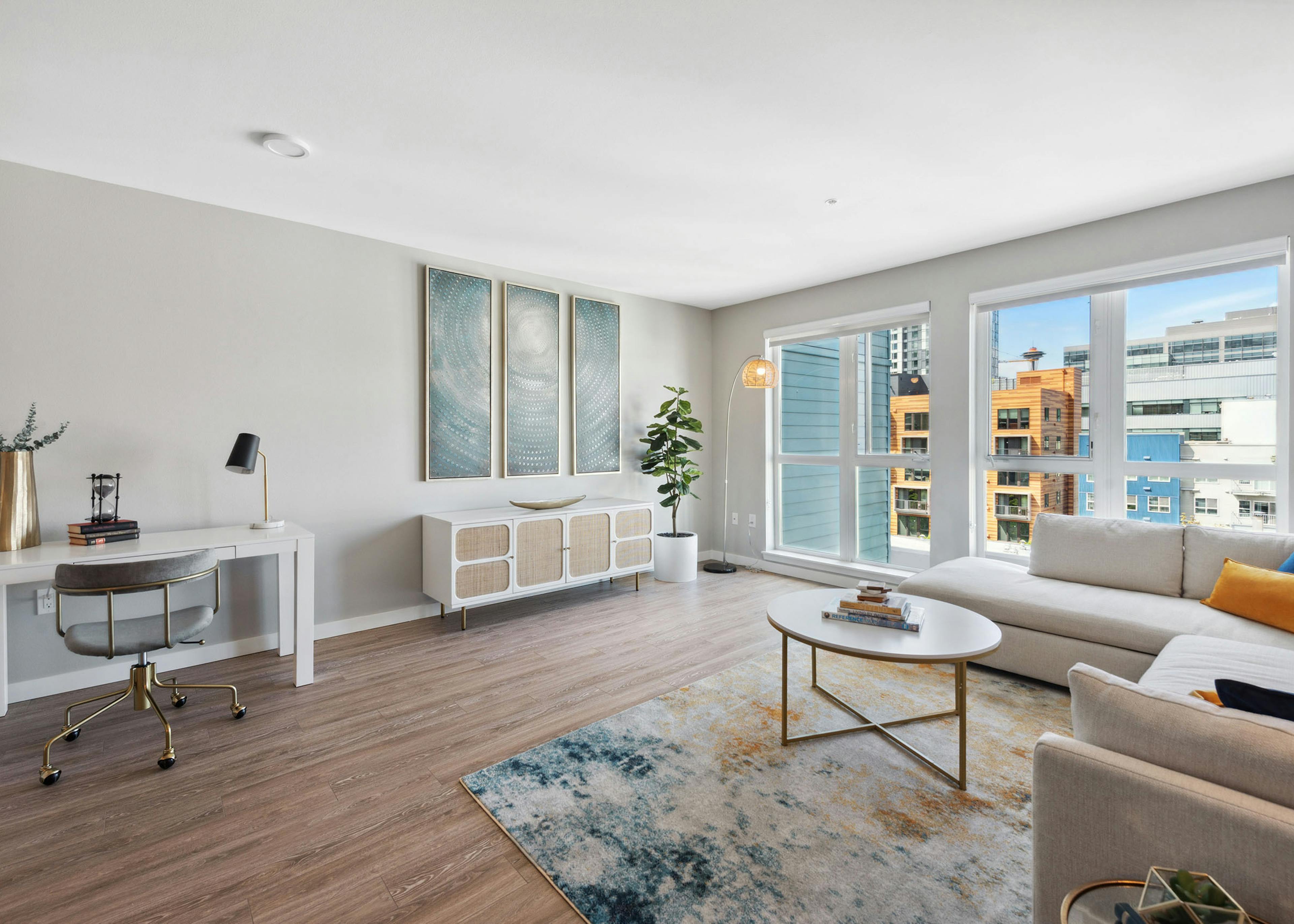 AMLI 535 living room with view of city and desk and sideboard with artwork and couch and multi color carpet with coffee table
