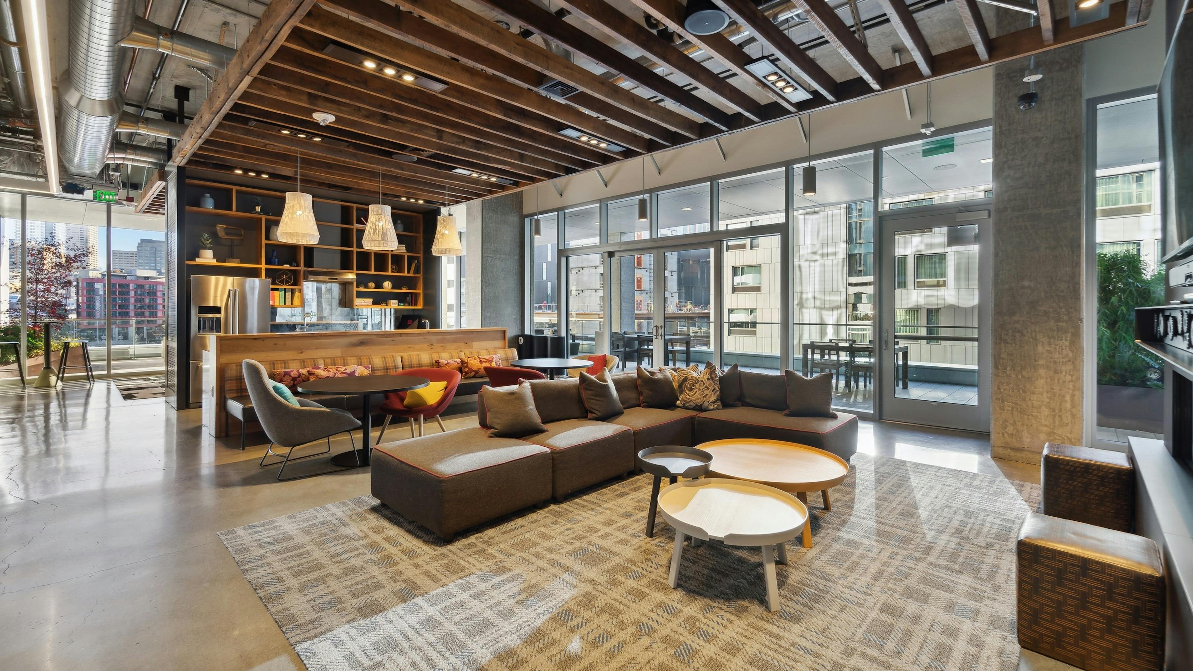 Interior clubroom of AMLI Arc with brown couch and other seating on area rug and kitchen and access to patio