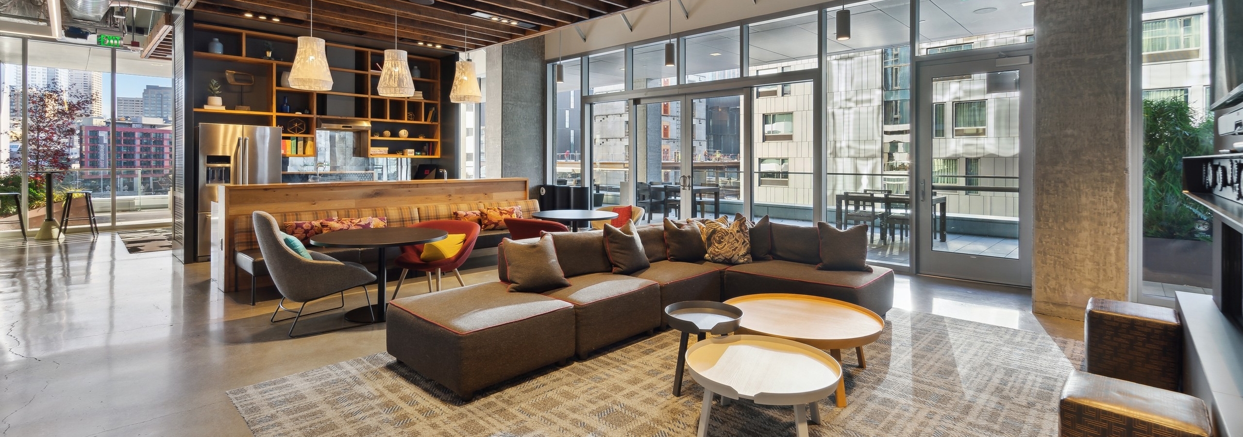Interior clubroom of AMLI Arc with brown couch and other seating on area rug and kitchen and access to patio