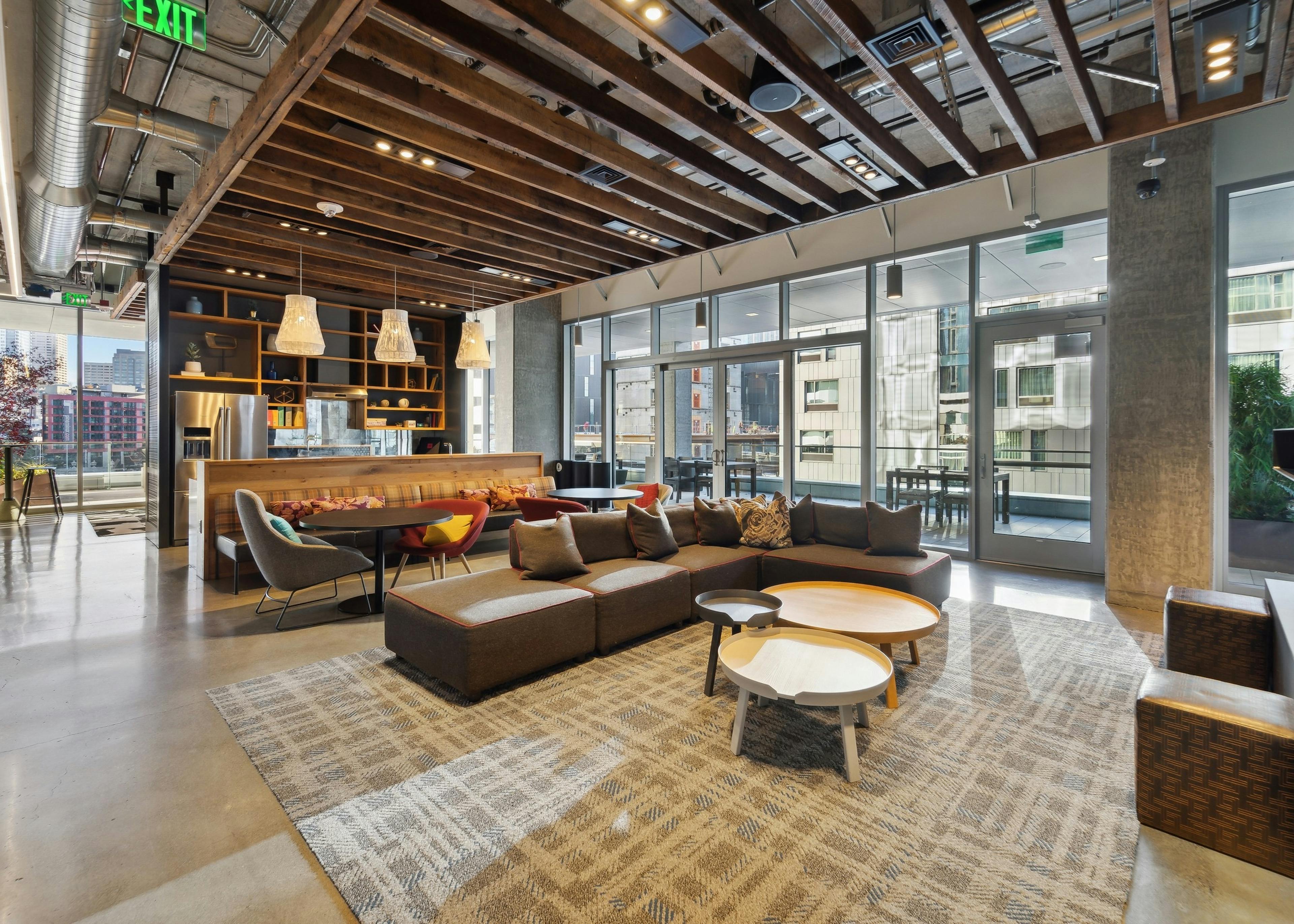 Interior clubroom of AMLI Arc with brown couch and other seating on area rug and kitchen and access to patio