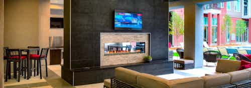 An outdoor fireplace at AMLI Denargo Market apartments with couches and a television with a slight view of the pool area