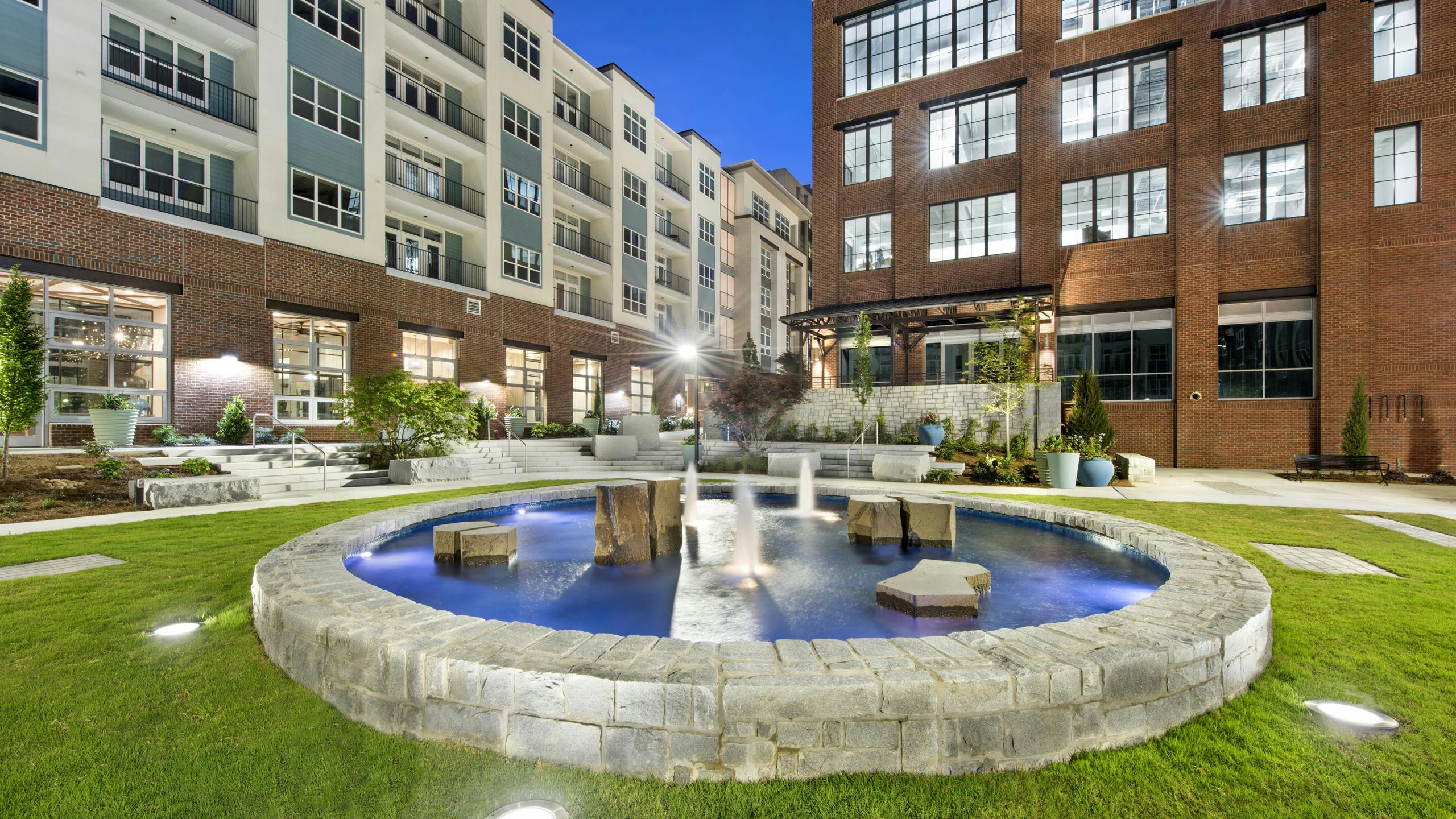 Nighttime view of the AMLI Decatur courtyard showcasing a lit stone fountain with blue water surrounded by manicured grass