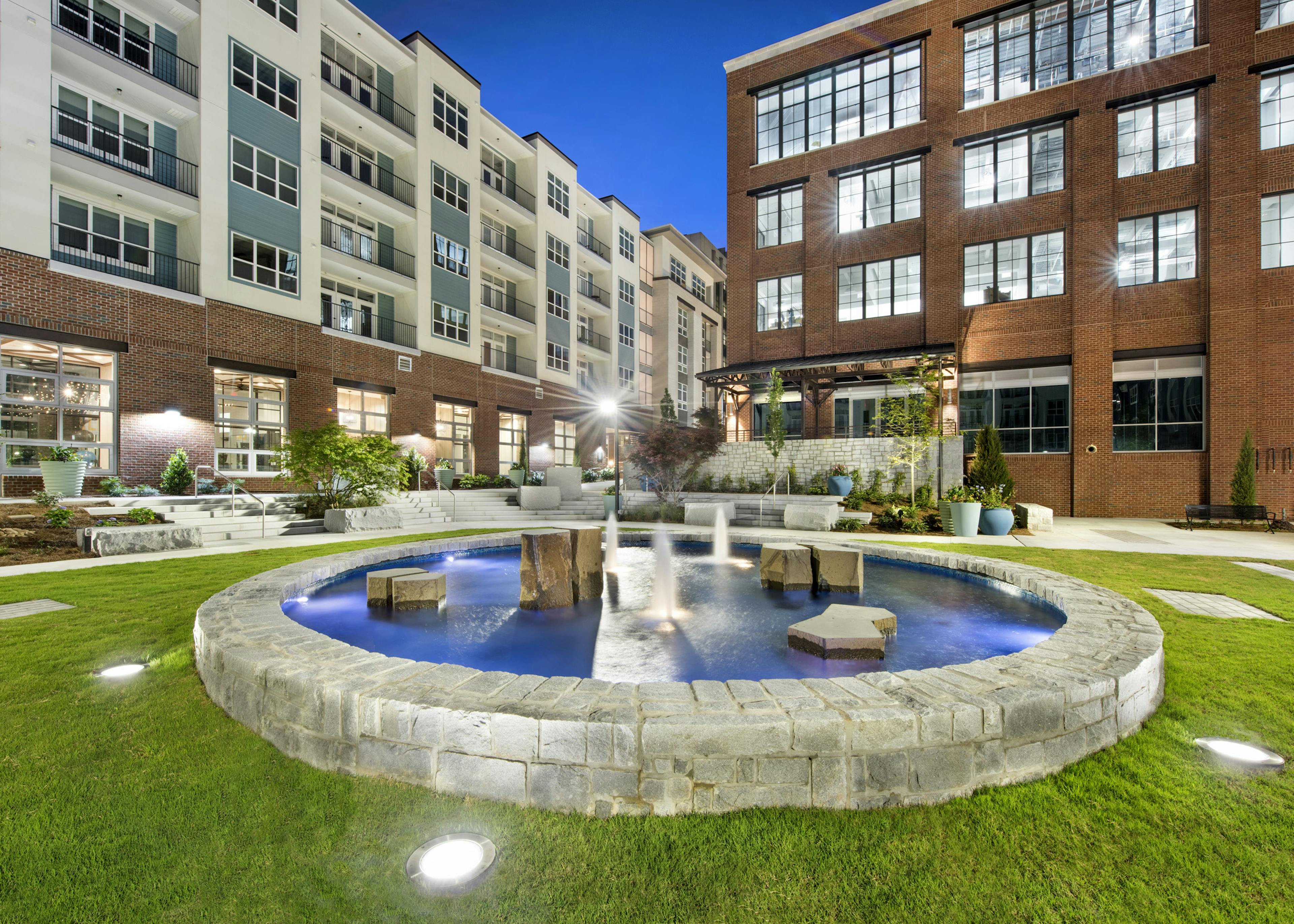 Nighttime view of the AMLI Decatur courtyard showcasing a lit stone fountain with blue water surrounded by manicured grass