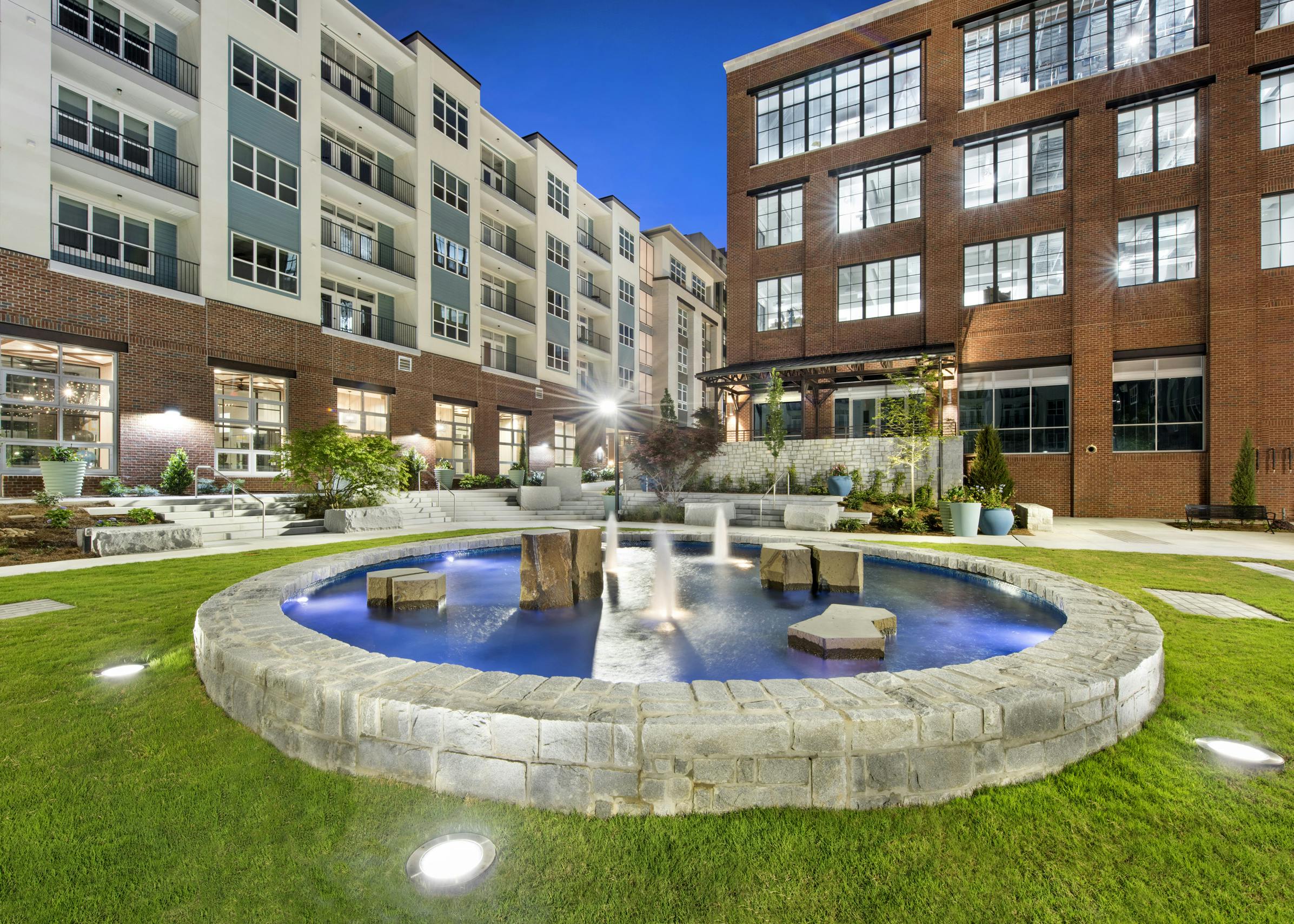 Nighttime view of the AMLI Decatur courtyard showcasing a lit stone fountain with blue water surrounded by manicured grass