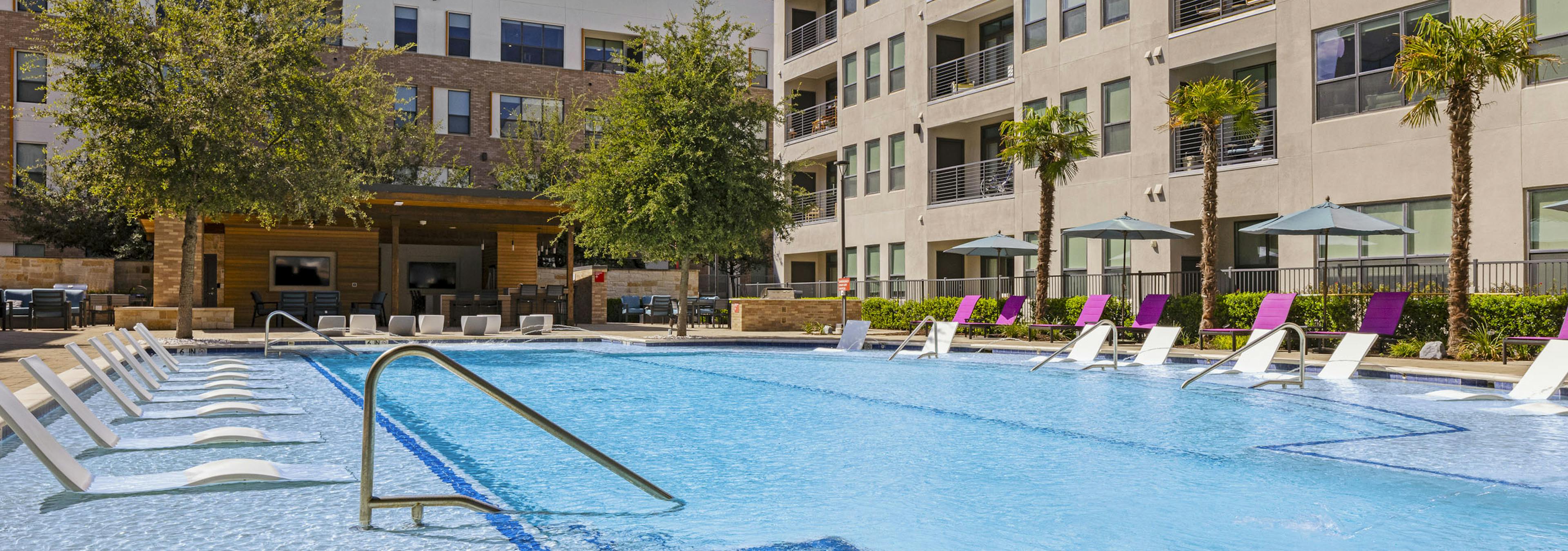 Daytime view of AMLI on Aldrich courtyard pool that is surrounded by tall palm trees and shaded lounge chairs