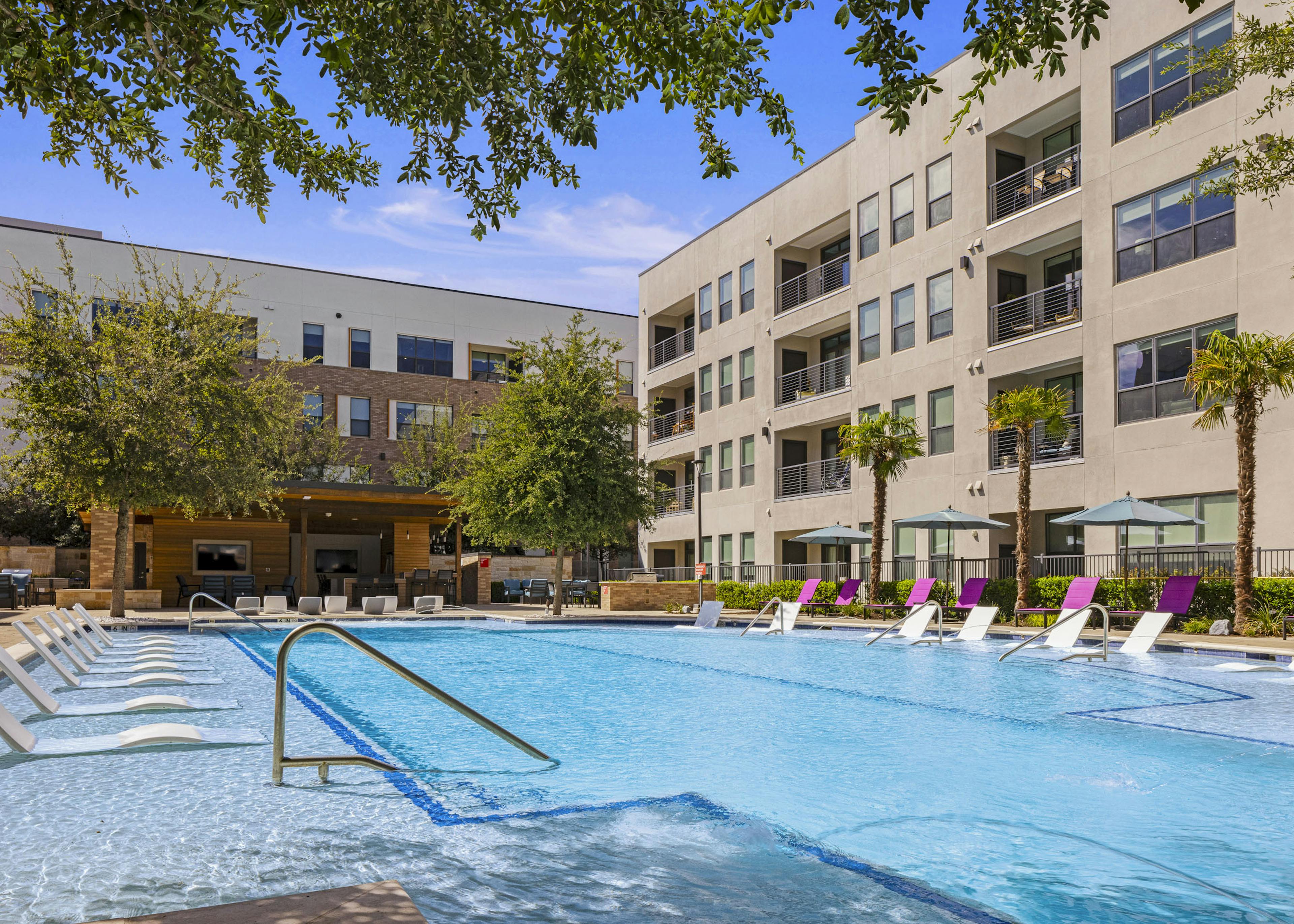 Daytime view of AMLI on Aldrich courtyard pool that is surrounded by tall palm trees and shaded lounge chairs