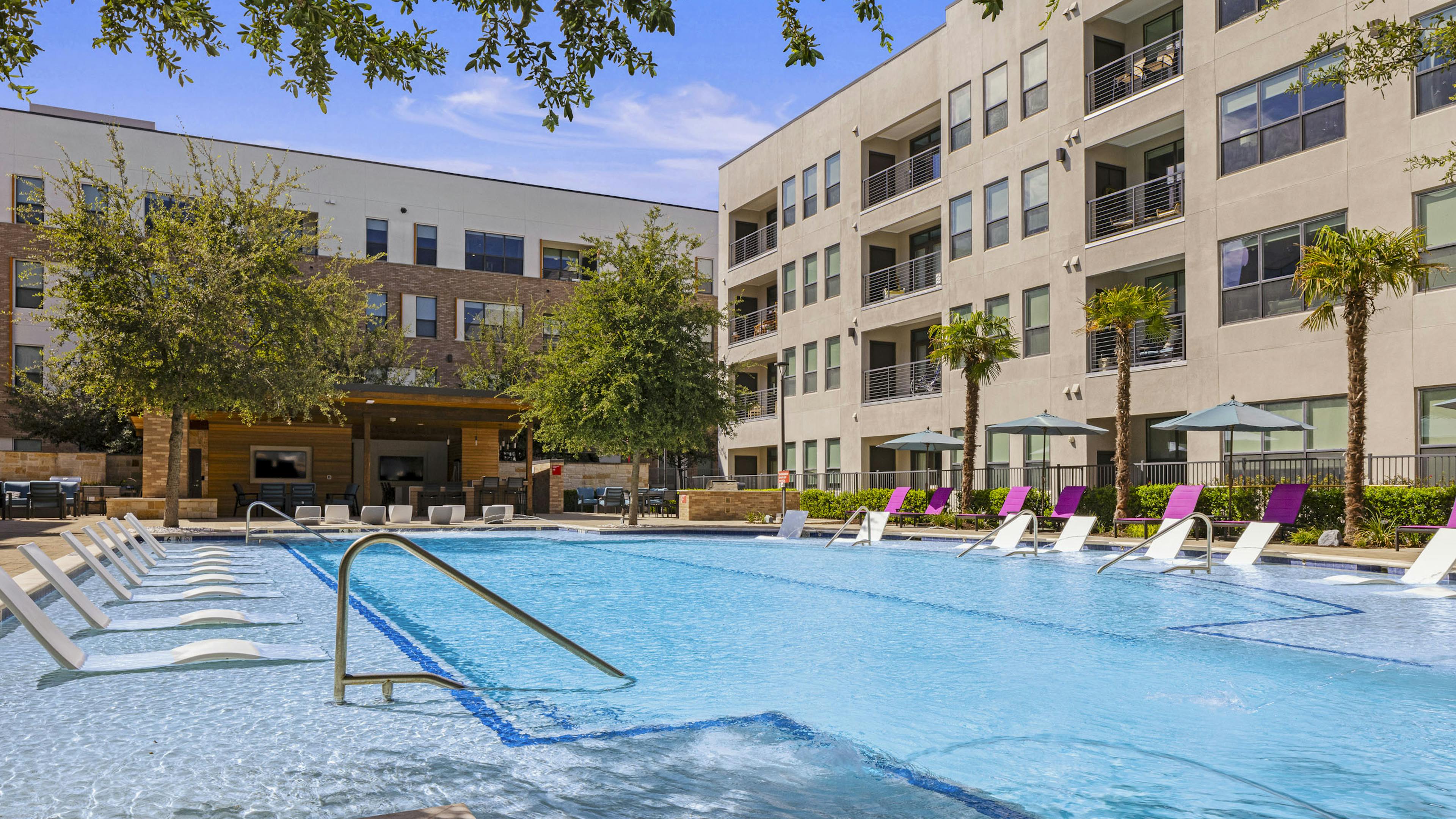 Daytime view of AMLI on Aldrich courtyard pool that is surrounded by tall palm trees and shaded lounge chairs