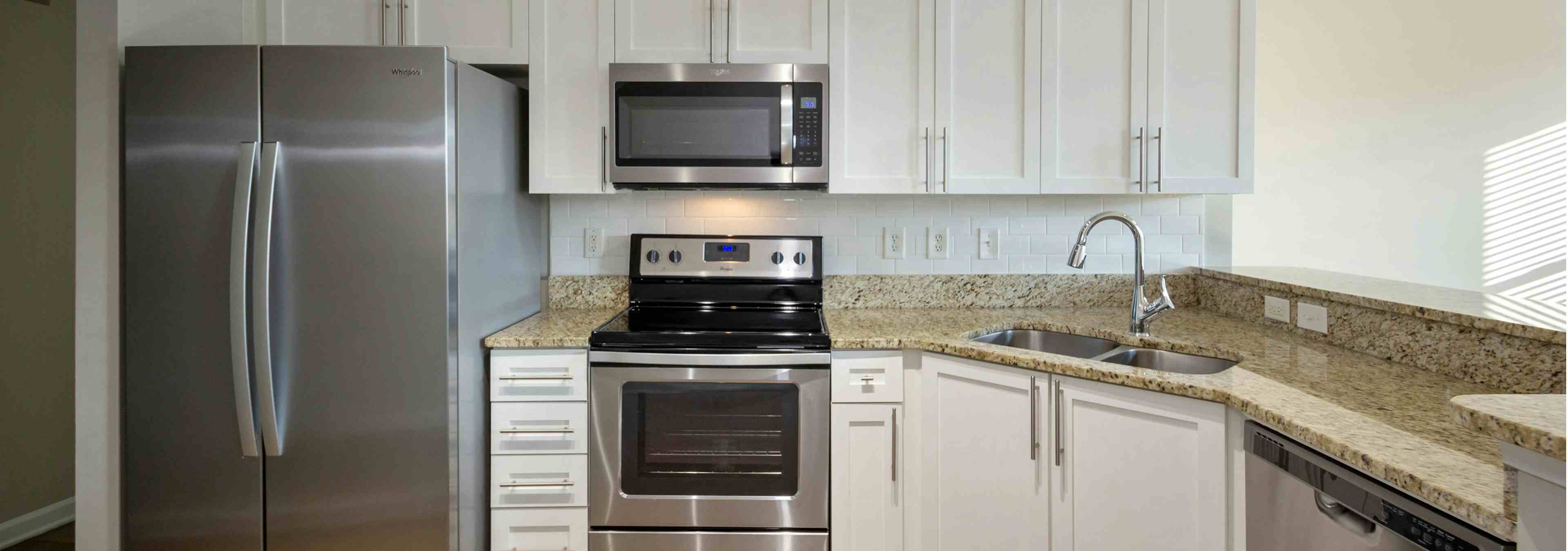 Close up of AMLI Lindbergh apartment kitchen with white cabinets, granite countertops, and stainless steel appliances