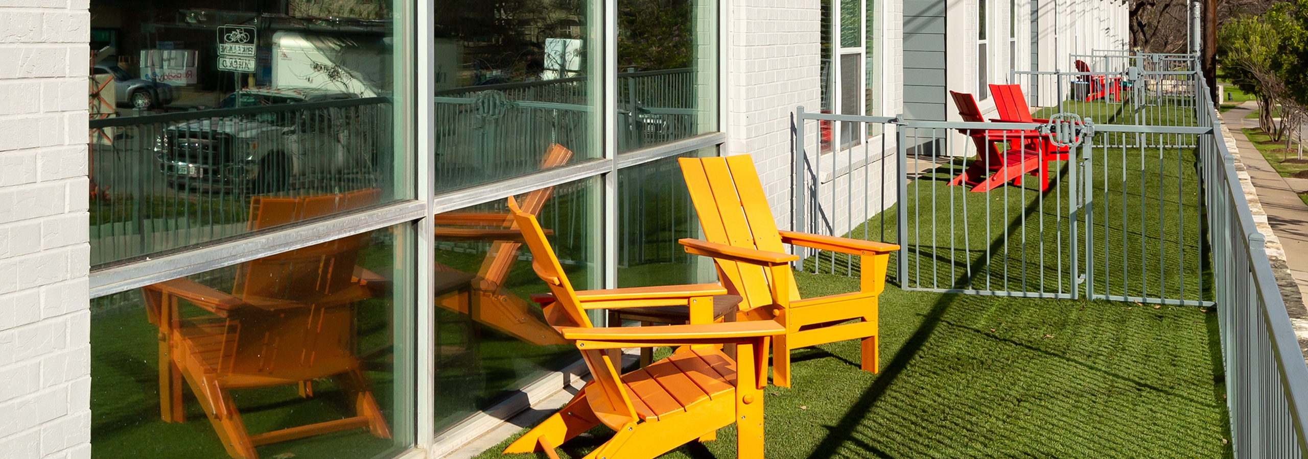 Exterior close up of a small fenced in apartment yard at AMLI South Shore with green turf and two orange lounge chairs