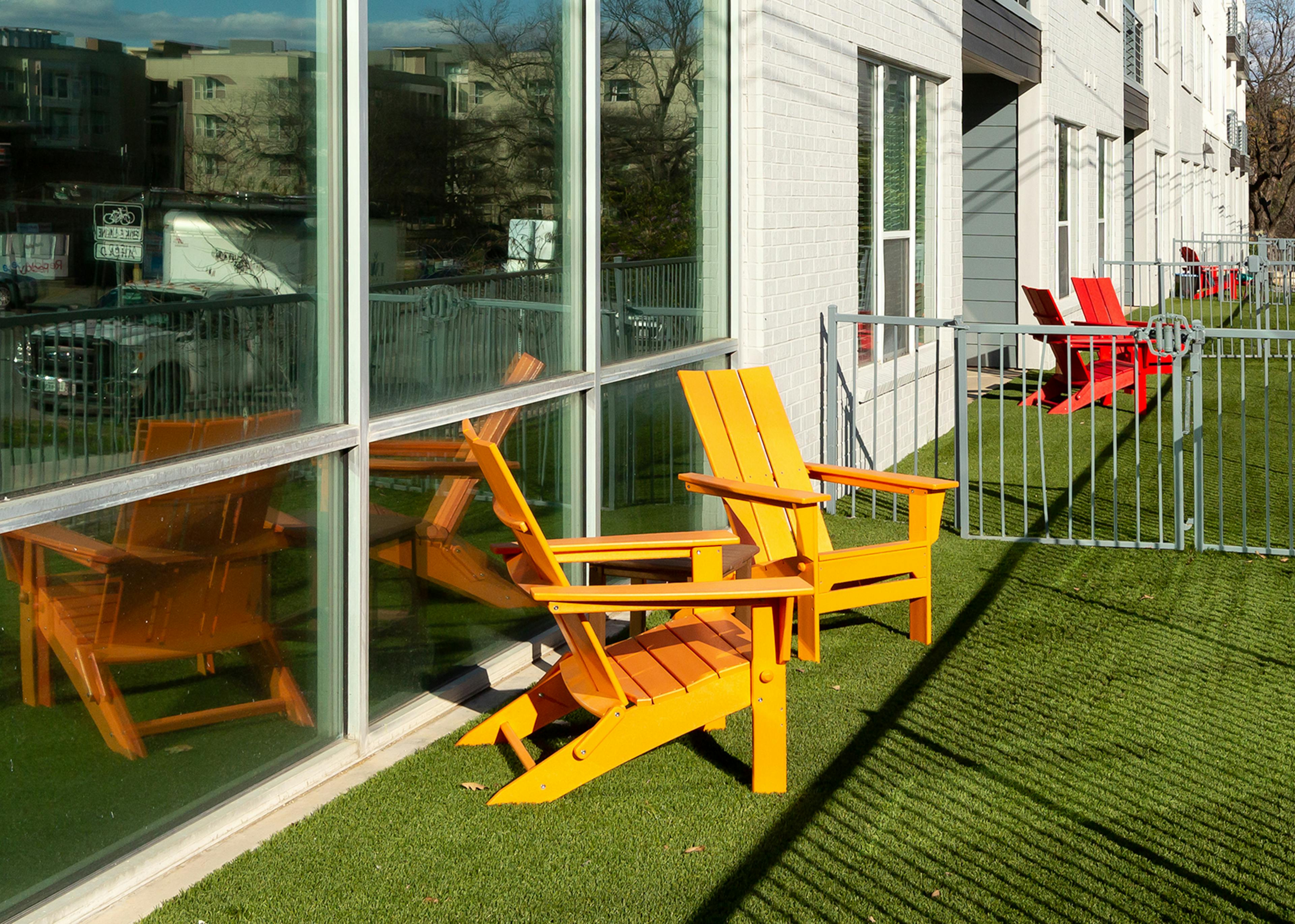 Exterior close up of a small fenced in apartment yard at AMLI South Shore with green turf and two orange lounge chairs