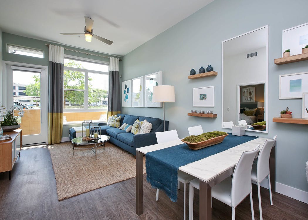 Interior view of AMLI Uptown Orange furnished apartment living room and dining area with blue couch in front of large windows