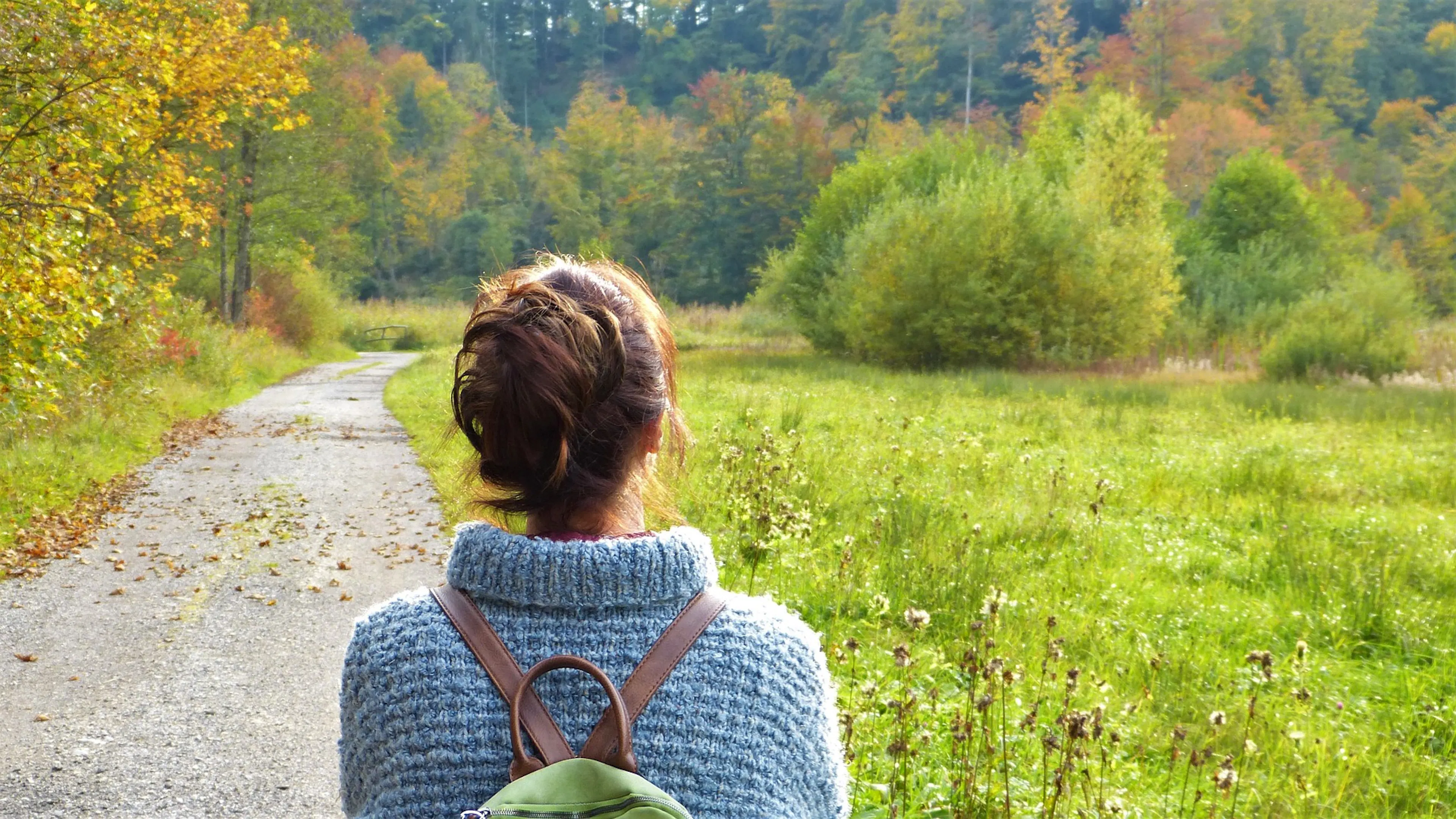 woman in sweater with backpack in green field on path
