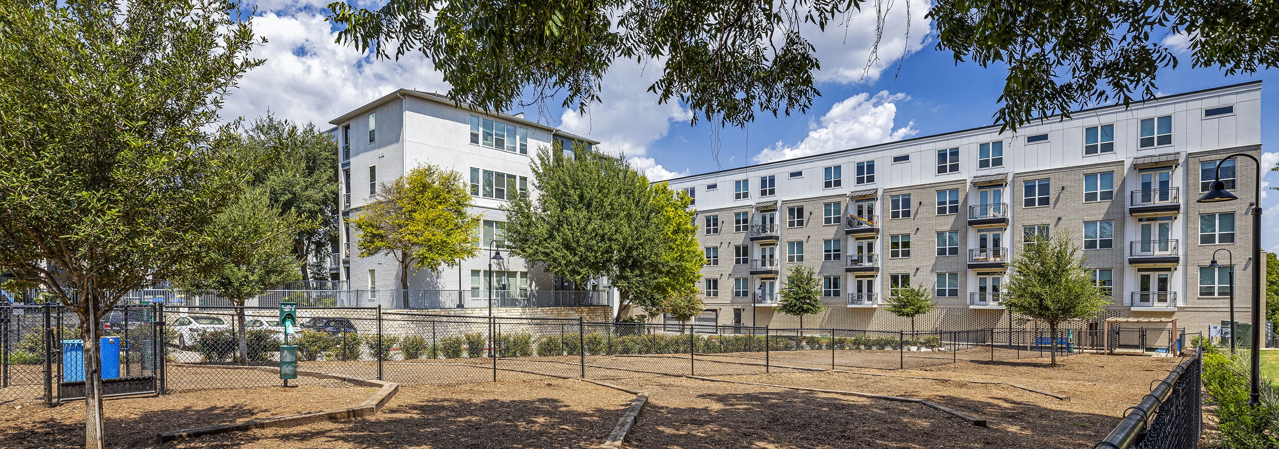 Fenced in pet park in front of AMLI South Shore apartment building with brown mulch and trees around