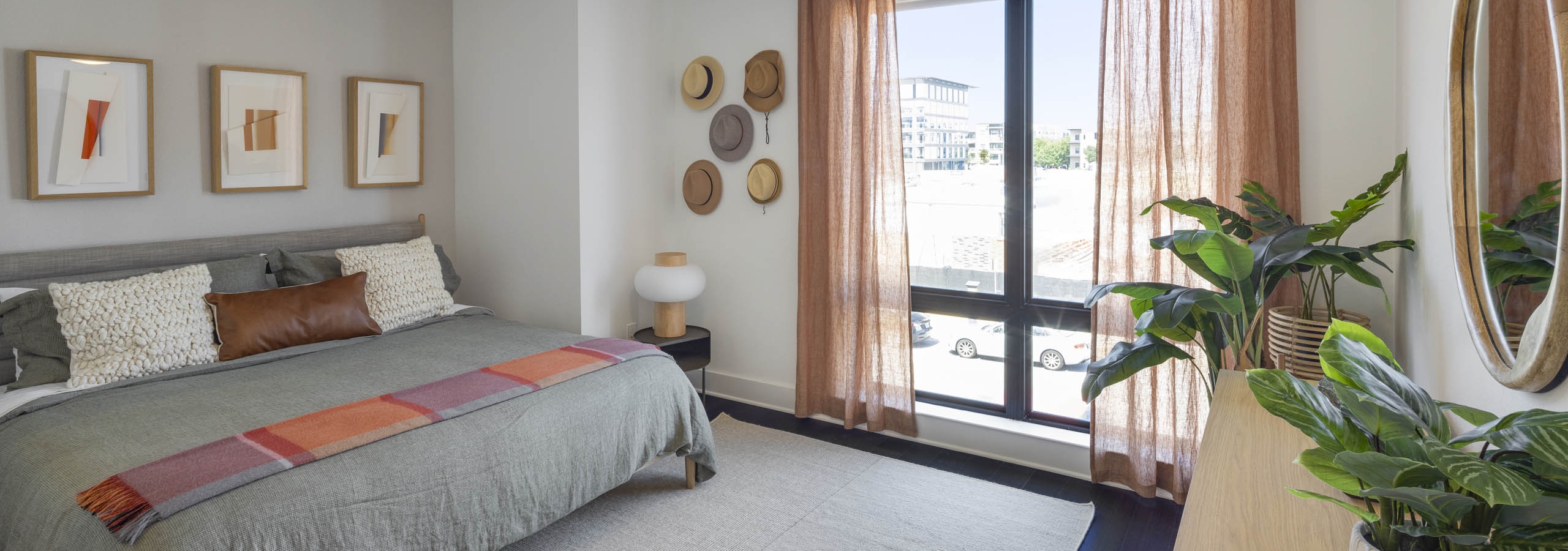 Bedroom with king size bed with grey bedding with rust accents and curtains and hats on wall at AMLI Branch Park apartments