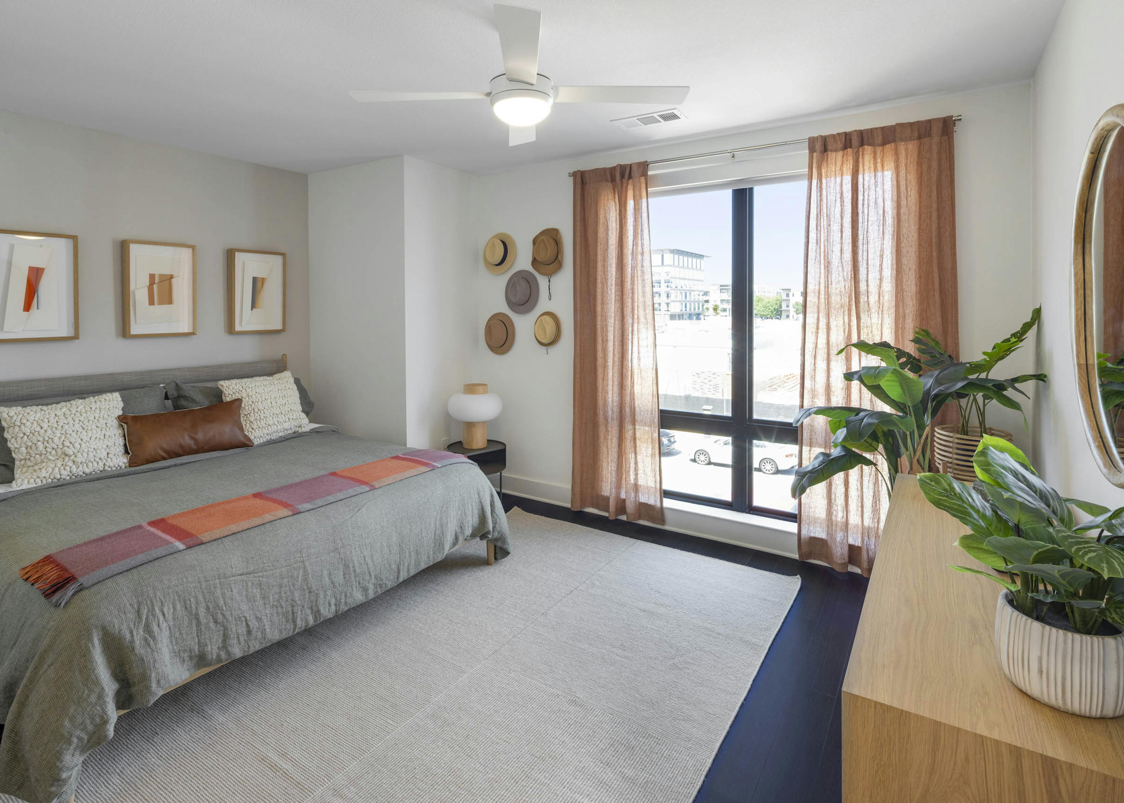 Bedroom with king size bed with grey bedding with rust accents and curtains and hats on wall at AMLI Branch Park apartments