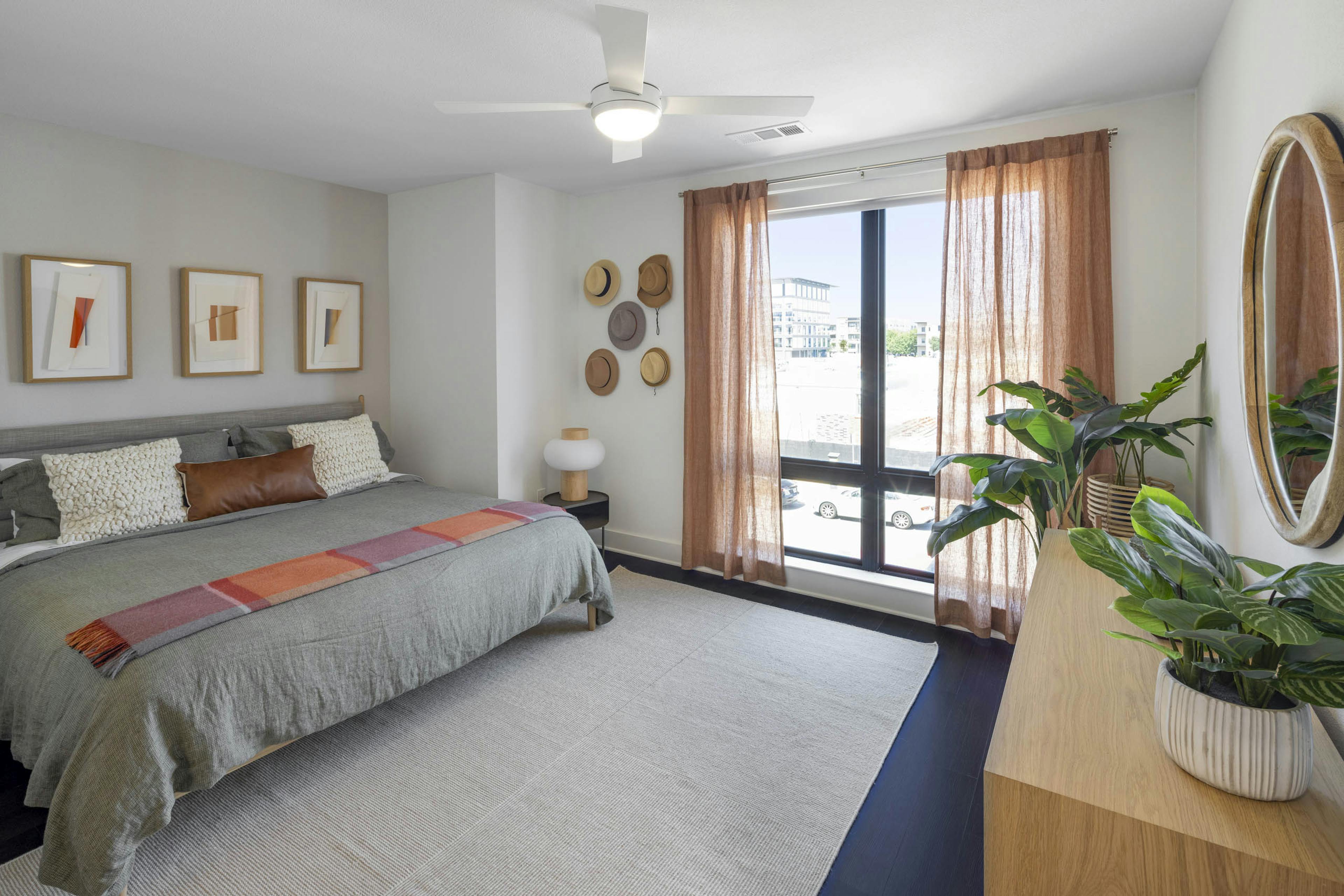 Bedroom with king size bed with grey bedding with rust accents and curtains and hats on wall at AMLI Branch Park apartments