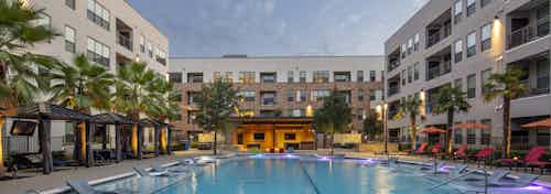 Dusk view of courtyard pool at AMLI on Aldrich apartments circled by private cabanas and palm trees and red lounge chairs