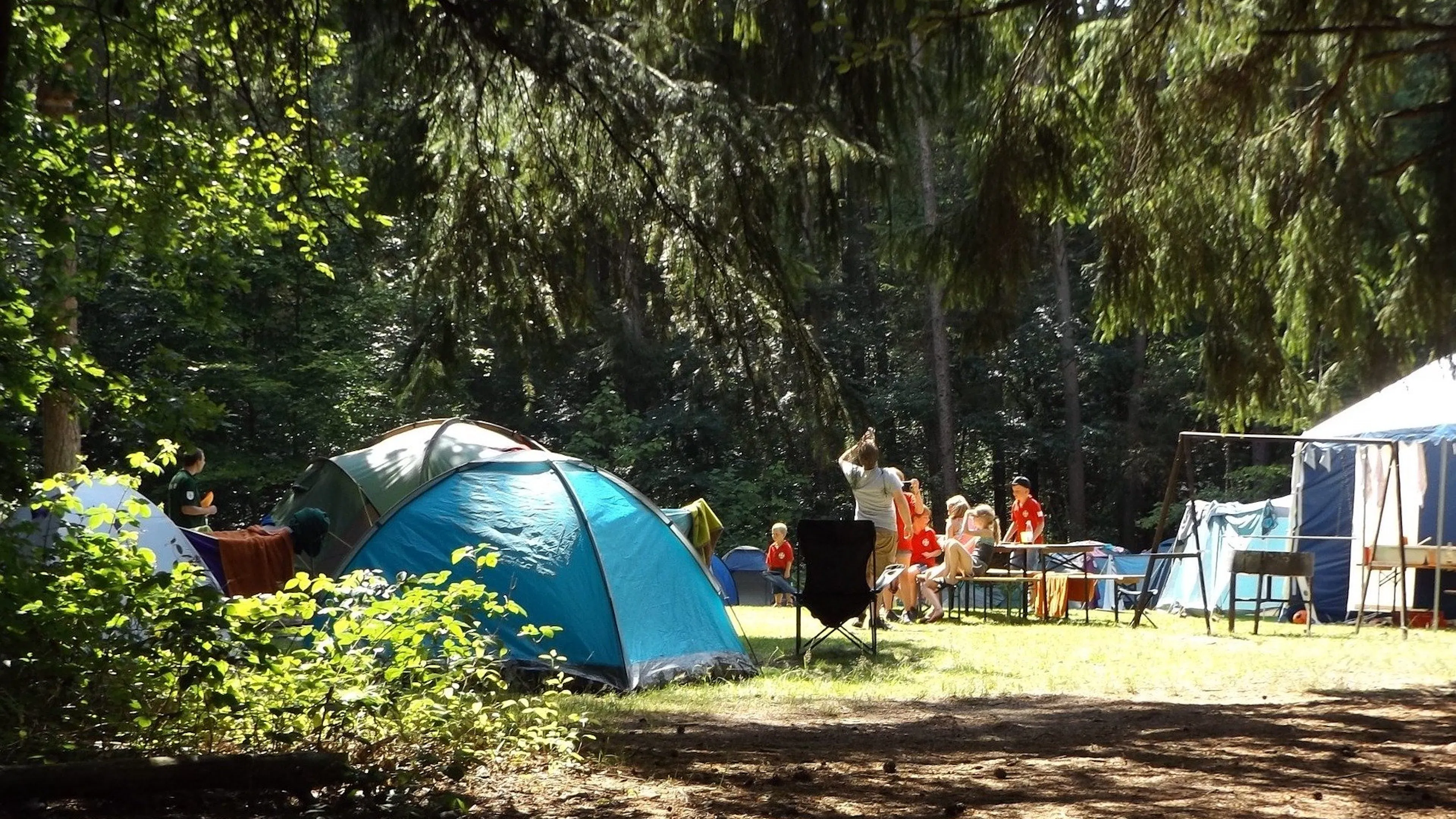 A collection of camping tents in a small clearing with people milling about