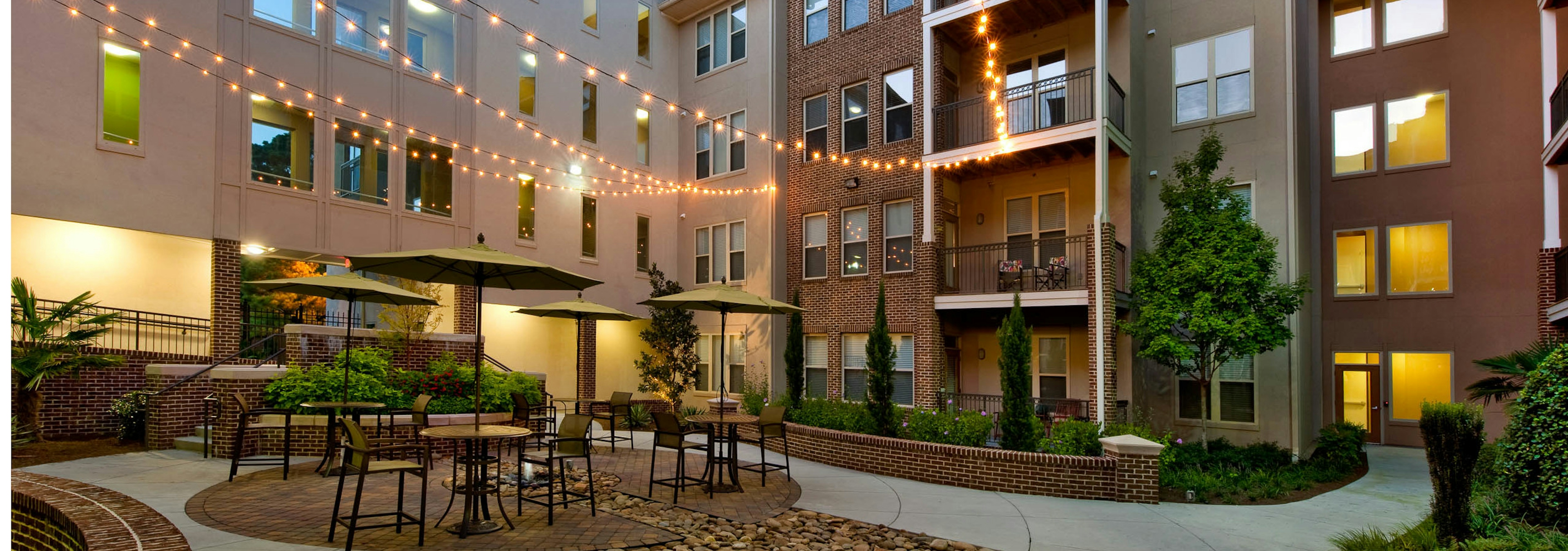 Exterior dusk view of AMLI Lindbergh courtyard on concrete with multiple table and chairs with umbrellas and hanging lights