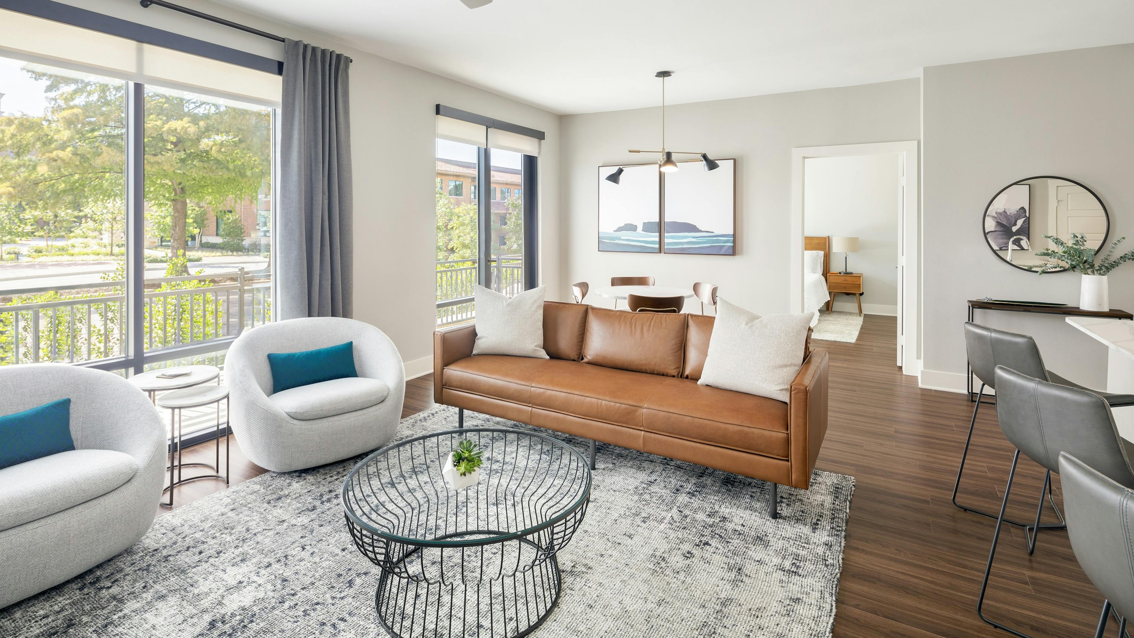 Guest suite with brown leather couch and two white chairs and coffee table near large windows at AMLI Addison apartments