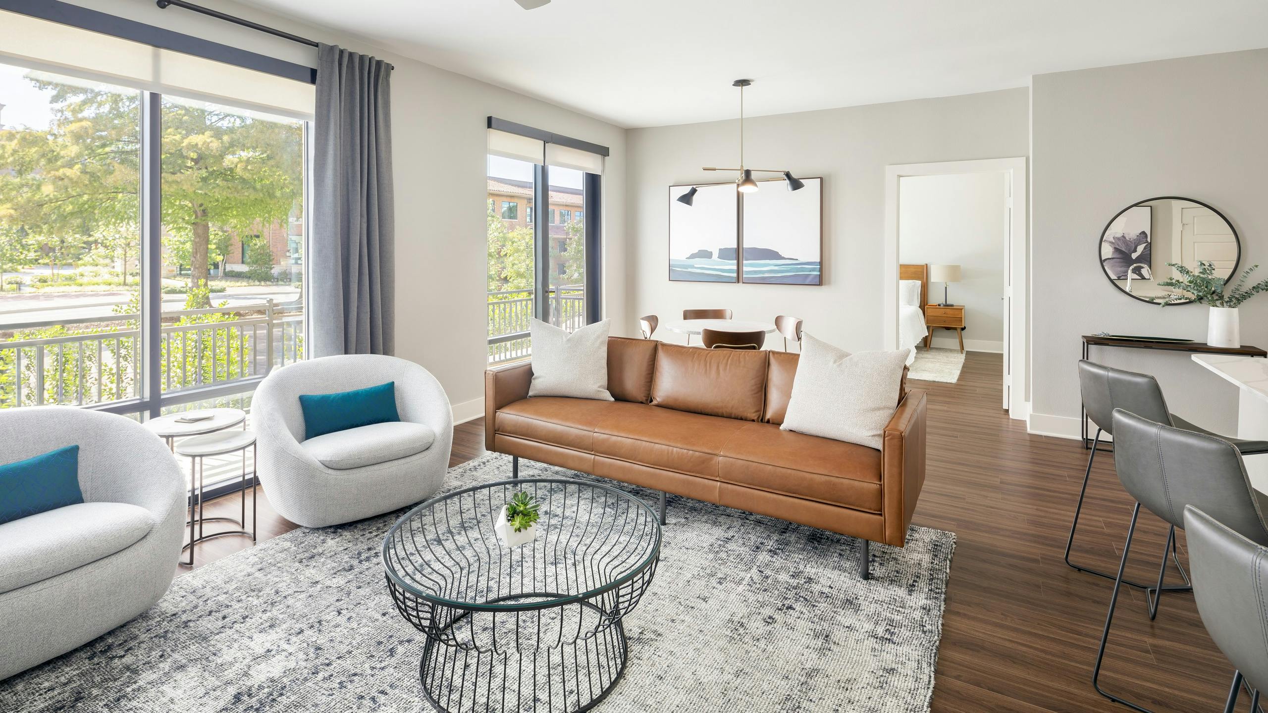 Guest suite with brown leather couch and two white chairs and coffee table near large windows at AMLI Addison apartments