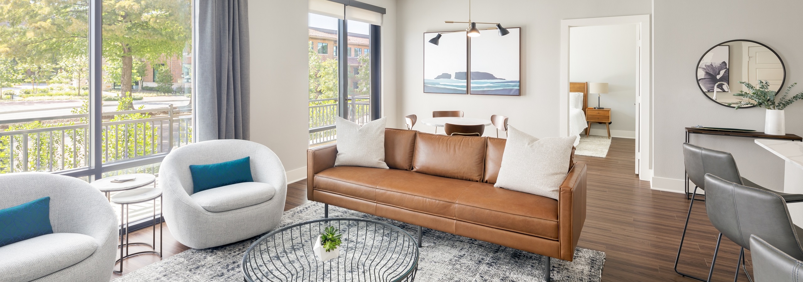 Guest suite with brown leather couch and two white chairs and coffee table near large windows at AMLI Addison apartments