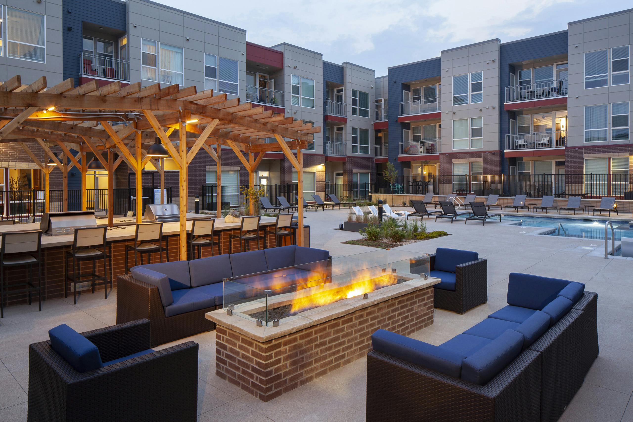 Nighttime view at AMLI Littleton Village fire pit surrounded by couches and chairs with the pool and grills in the background