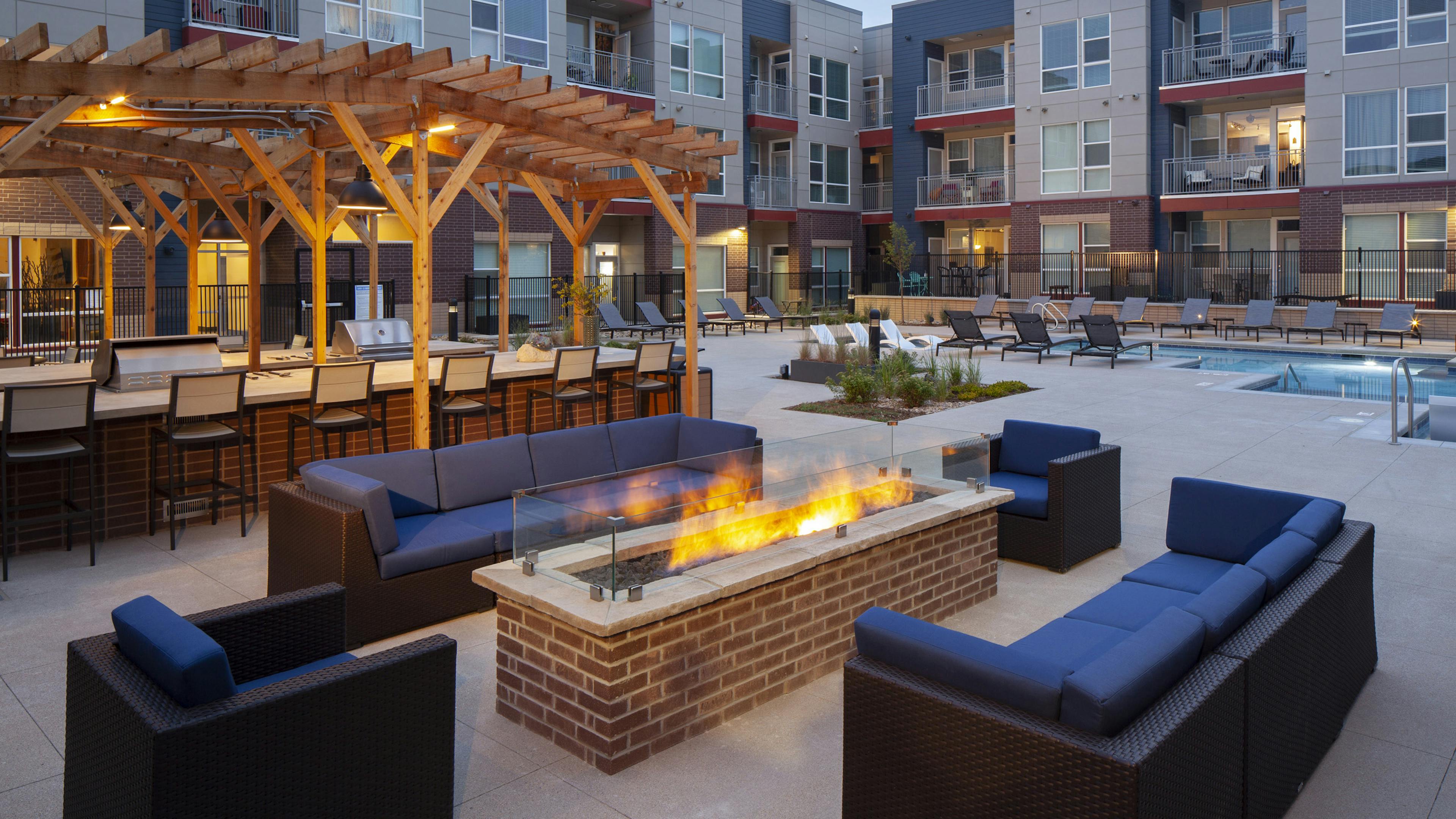 Nighttime view at AMLI Littleton Village fire pit surrounded by couches and chairs with the pool and grills in the background