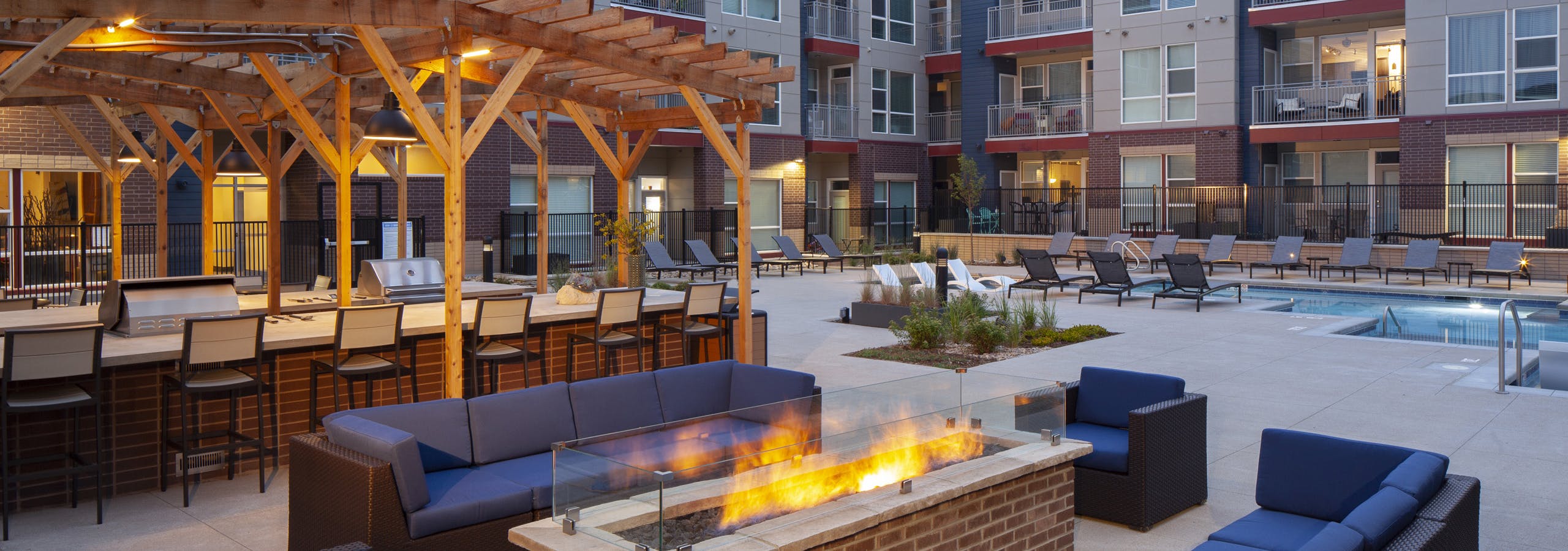 Nighttime view at AMLI Littleton Village fire pit surrounded by couches and chairs with the pool and grills in the background