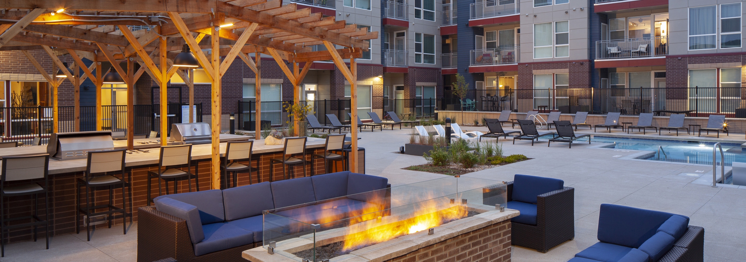 Nighttime view at AMLI Littleton Village fire pit surrounded by couches and chairs with the pool and grills in the background