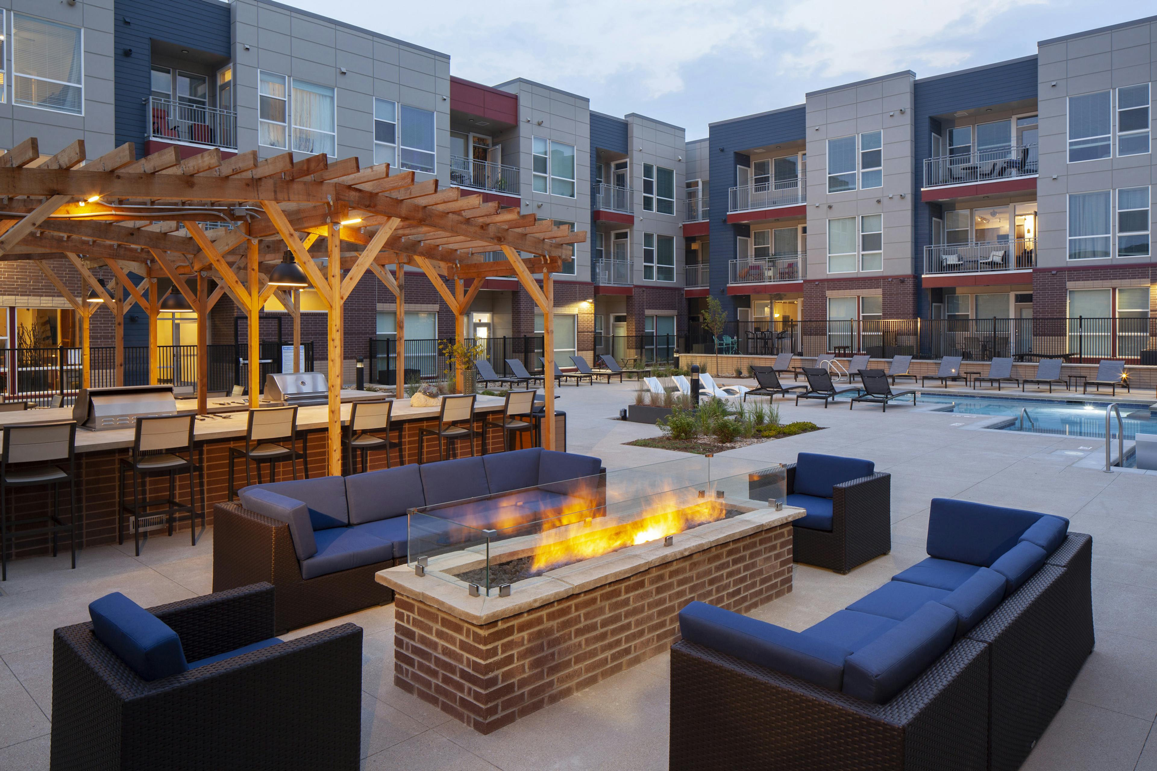 Nighttime view at AMLI Littleton Village fire pit surrounded by couches and chairs with the pool and grills in the background