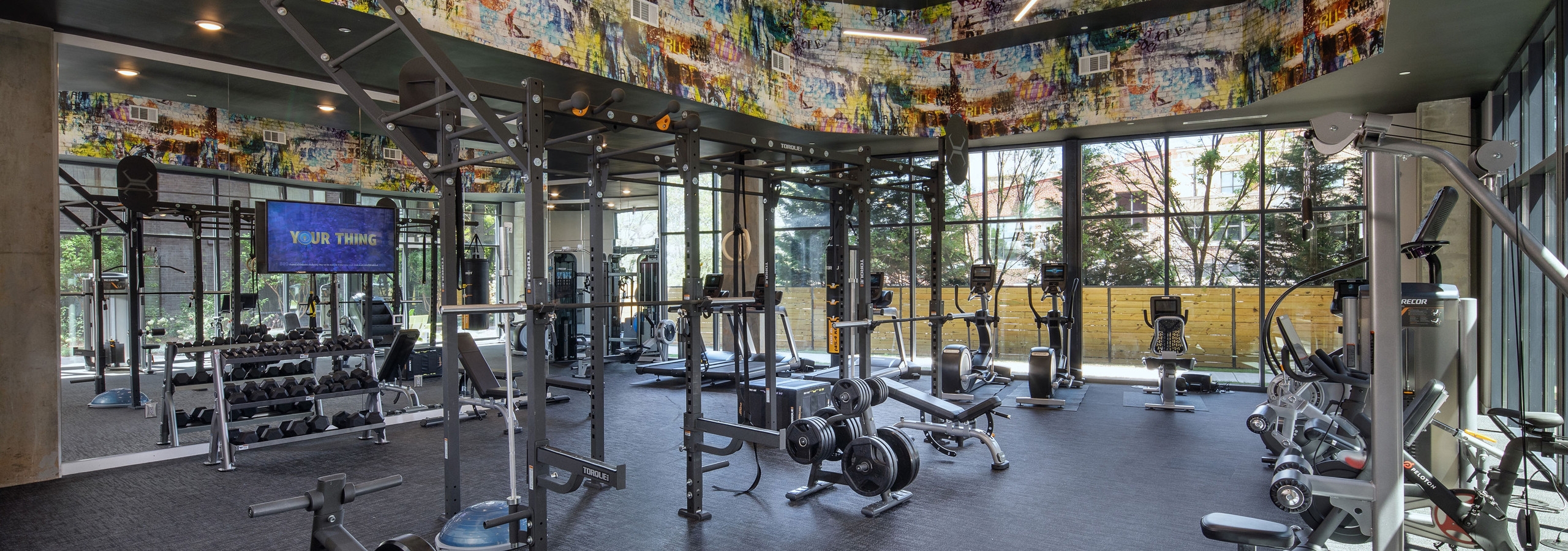 AMLI Westside apartment fitness studio with various weight machines and a free weight station with windows looking outside