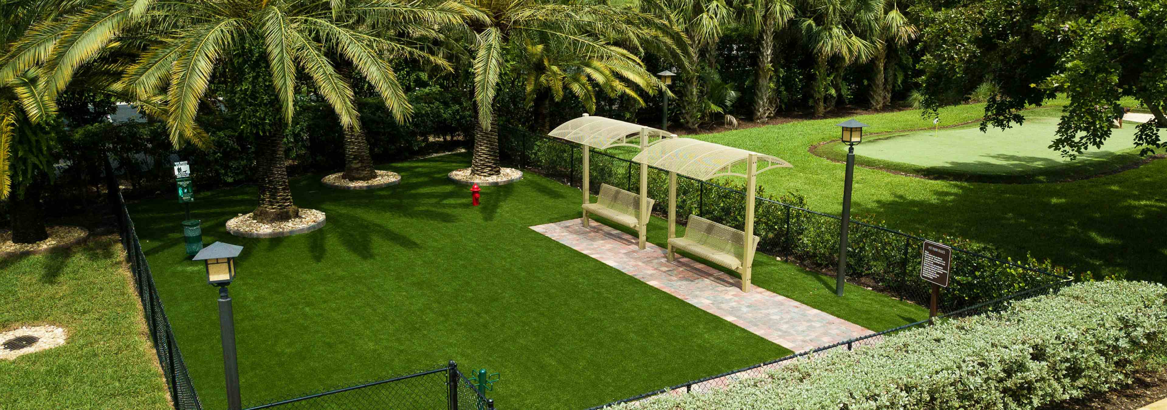 Daytime aerial view of AMLI Toscana Place expansive Paw Park with faux grass, lush landscape and covered benches