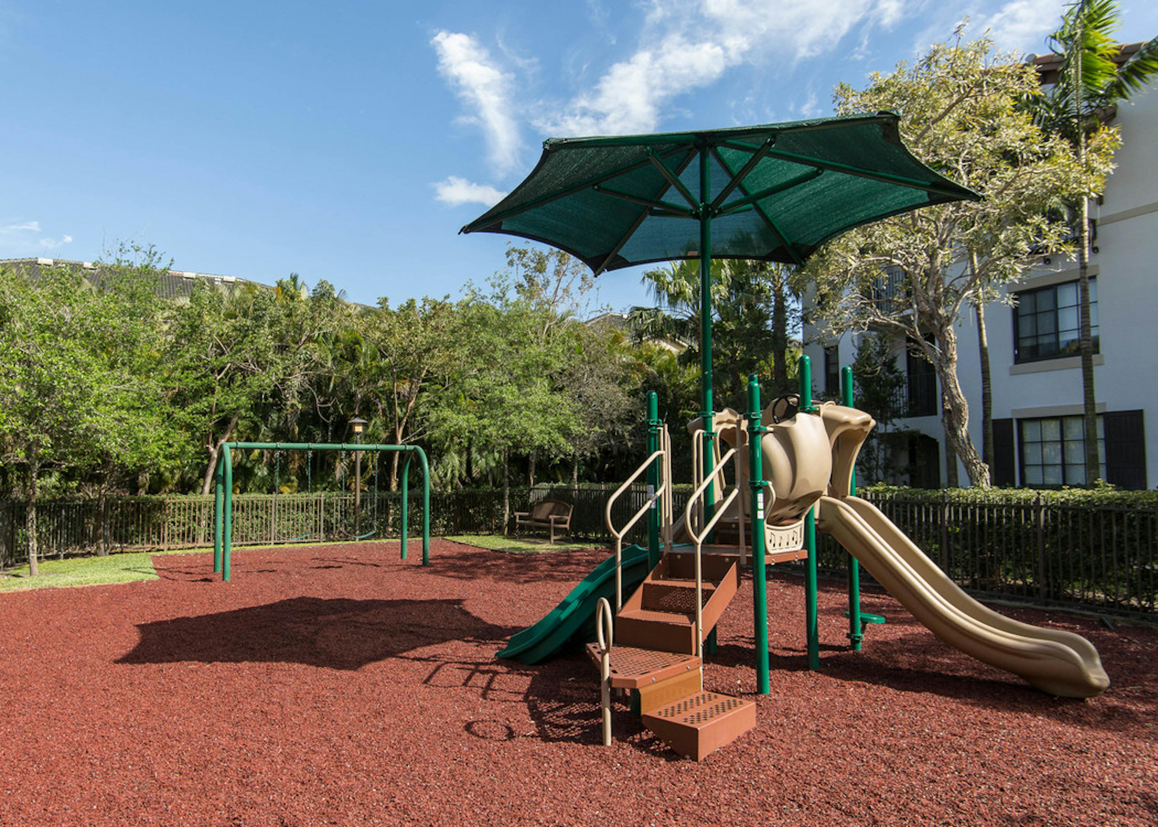 Outdoor children’s playground at AMLI Toscana Place featuring stairs for climbing, slide and swings all set on rubber floor