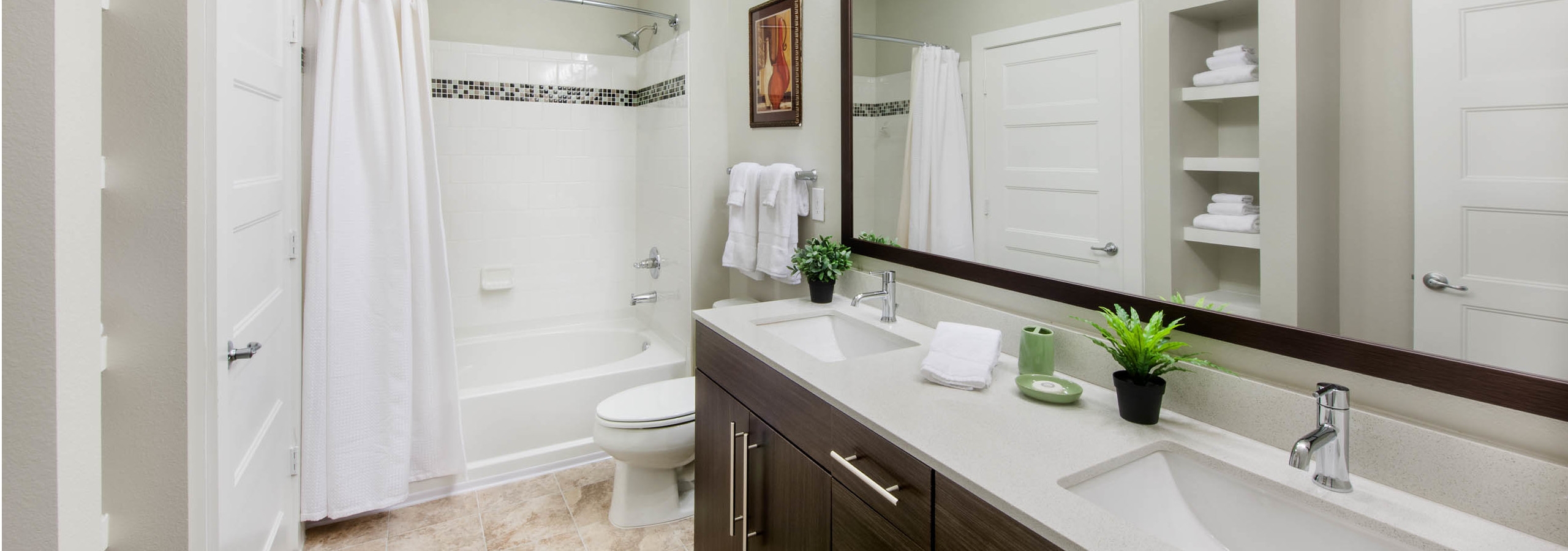 Interior of AMLI Piedmont Heights bathroom with a double dark wood vanity and mirror with a toilet and white shower tub