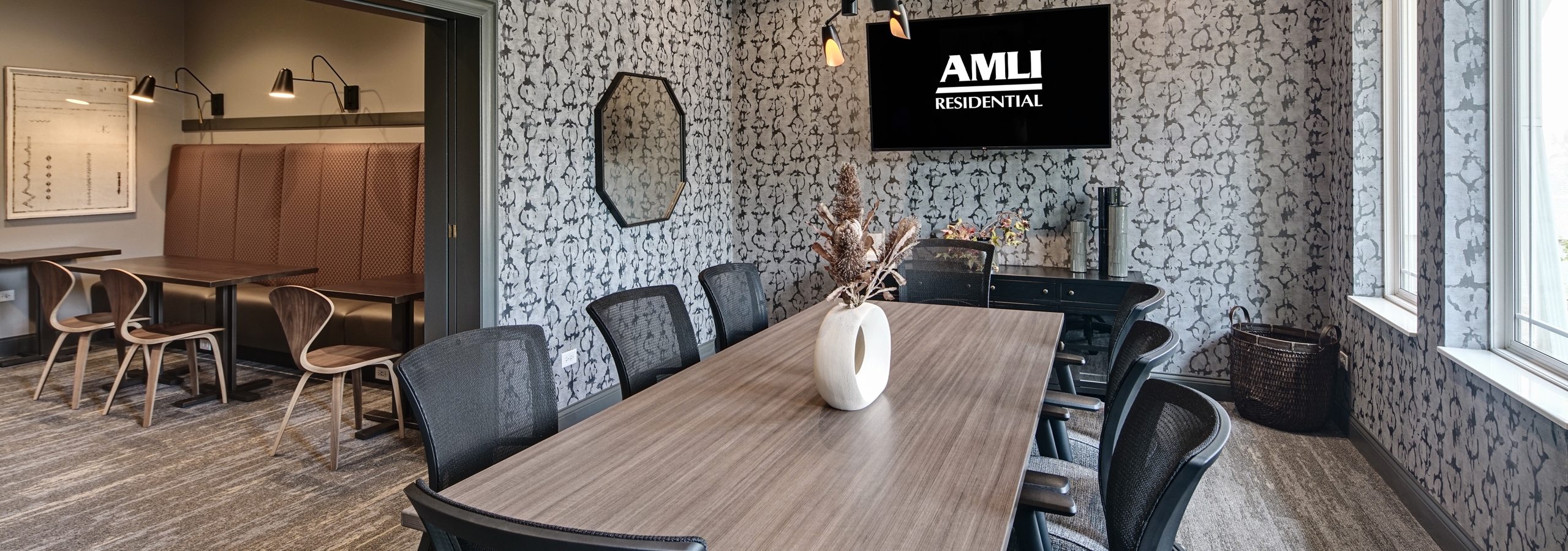 Conference room at AMLI at Seven Bridges apartments with long wood grain table and 8 gray chairs and gray and white wallpaper